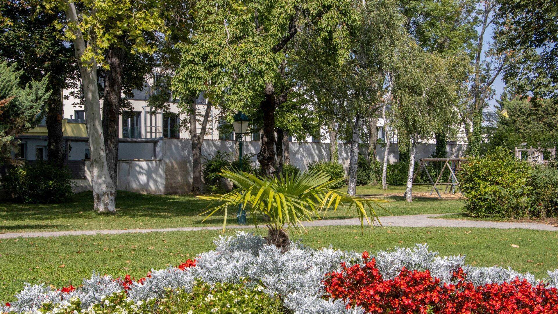 Gepflegter Gartenbereich mit Blumenbeeten, Rasenflächen und hohen Bäumen, ideal zur Entspannung.