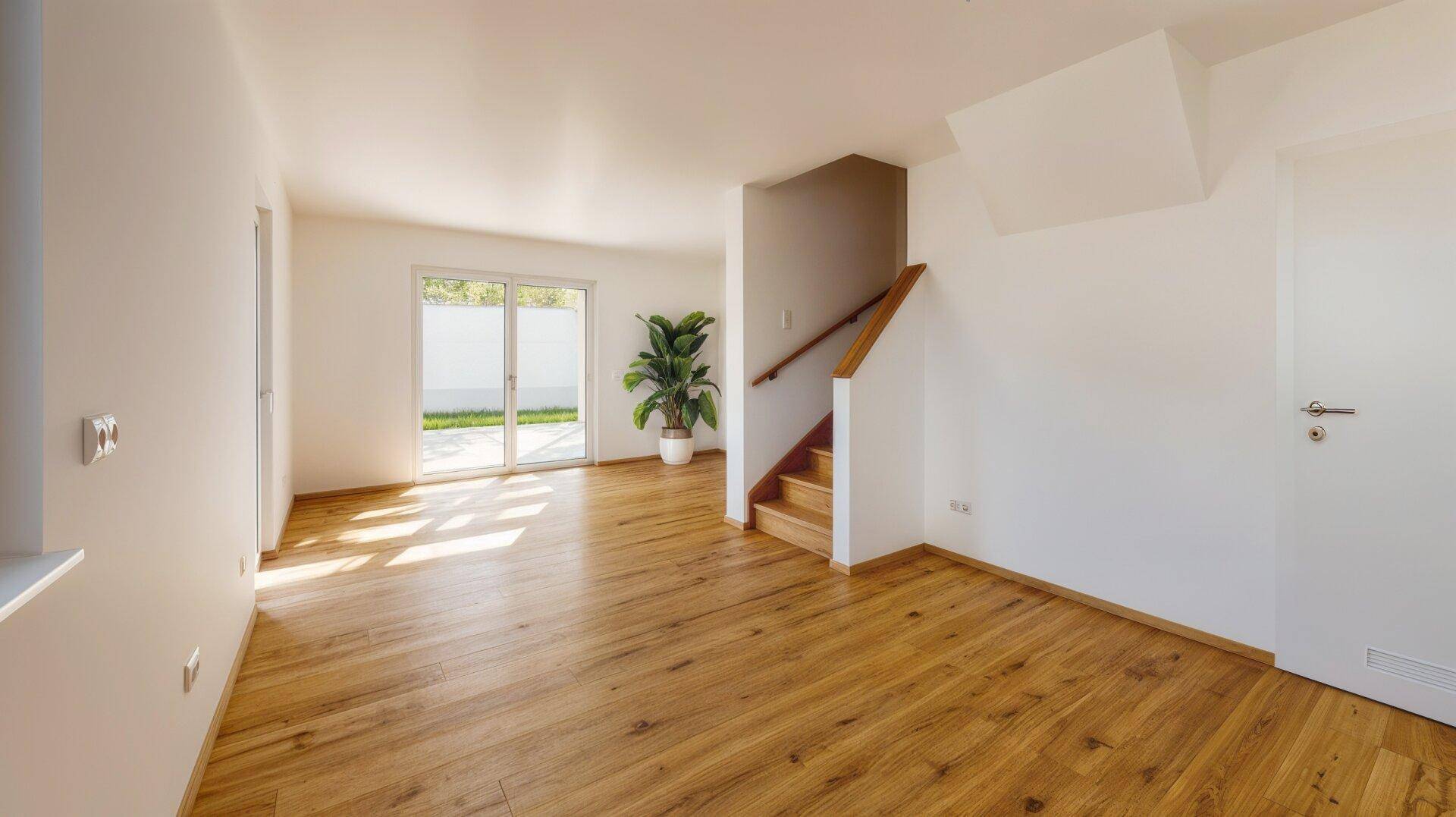 Geräumiger, leerer Raum mit Holzboden, Treppe und einer großen Zimmerpflanze.