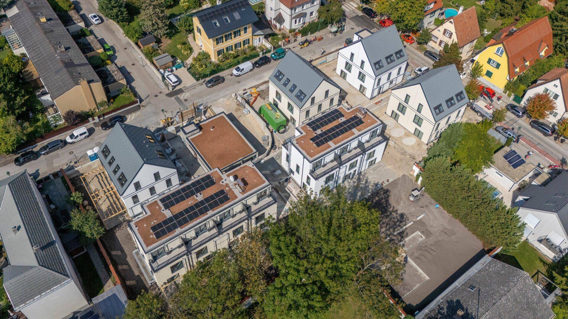 Luftaufnahme einer neuen Wohnsiedlung mit modernen Gebäuden und Photovoltaikanlagen auf den Dächern.