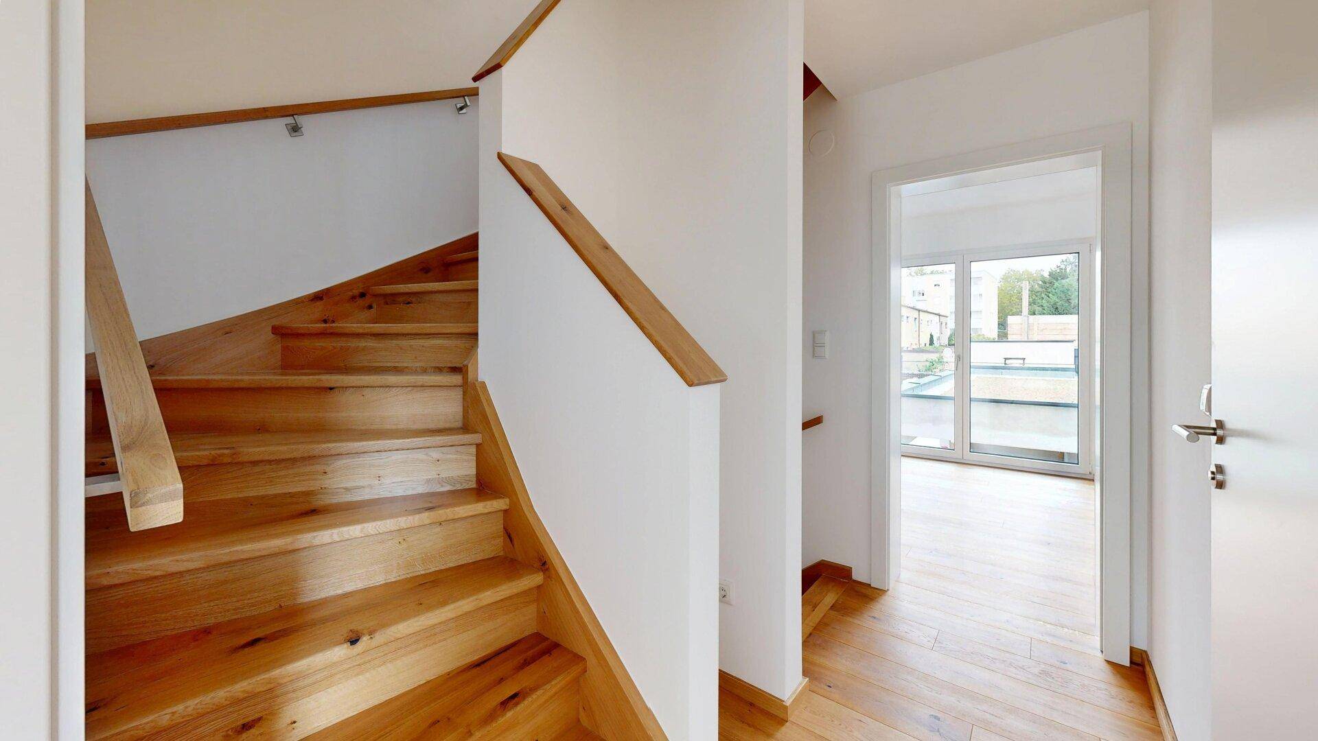 Heller Flur mit Holztreppe und Holzboden, der zu weiteren Räumen führt.