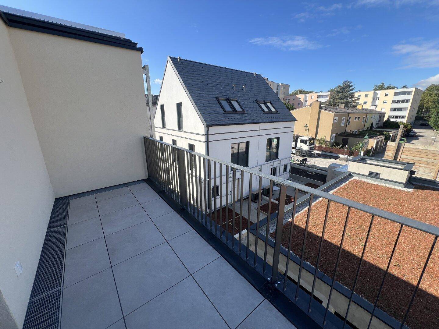 Geräumiger Balkon mit Fliesenboden und Blick auf umliegende Gebäude und Dächer.