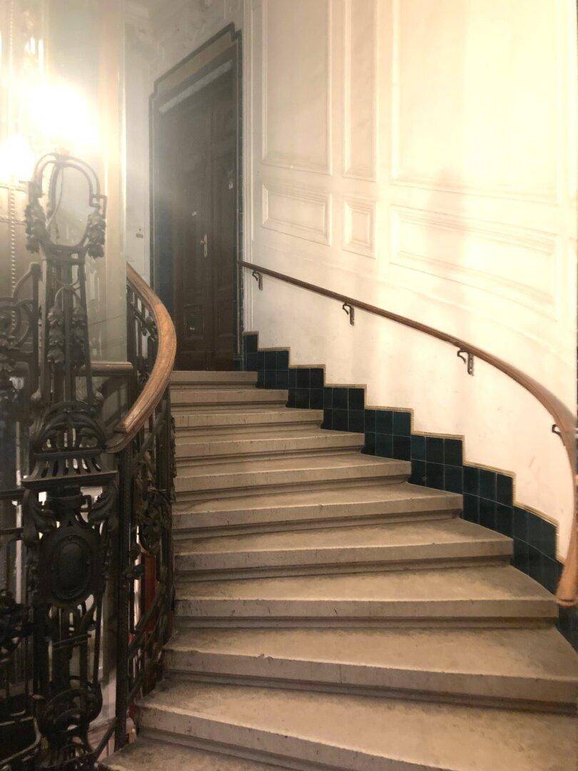 Historisches Treppenhaus mit schmiedeeisernem Geländer, Holzhandlauf und eleganten Stufen.