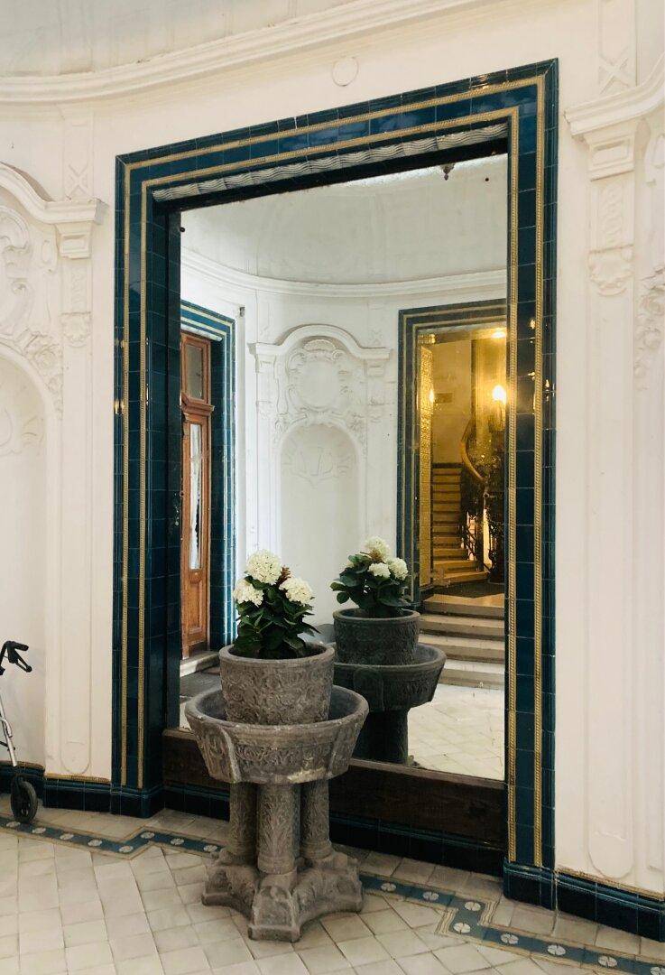Elegante Eingangshalle mit großem Spiegel, dekorativen Fliesen und einem verzierten Blumenständer.