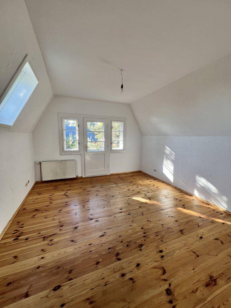 Leerer Raum mit Holzboden, Dachschräge und Zugang zu einem Außenbereich.