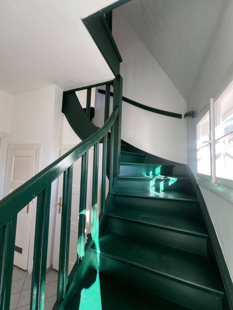 Geschwungene Holztreppe in dunkelgrün, führt zu den oberen Etagen des Hauses.