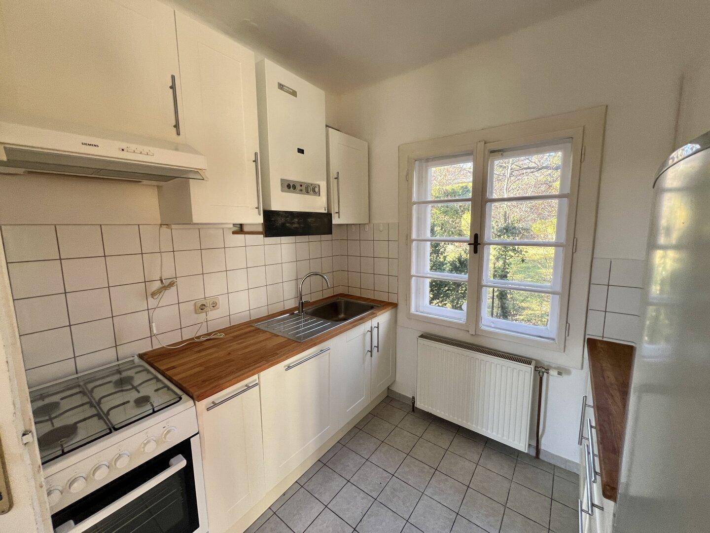 Kleine Küche mit weißen Schränken, Holztheke und Gasherd, Blick ins Grüne.