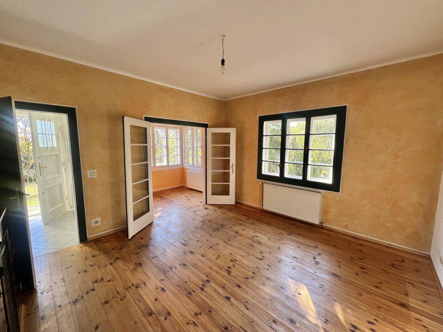 Geräumiger Raum mit Holzboden und orangefarbenen Wänden, bietet Zugang zu einem Außenbereich.
