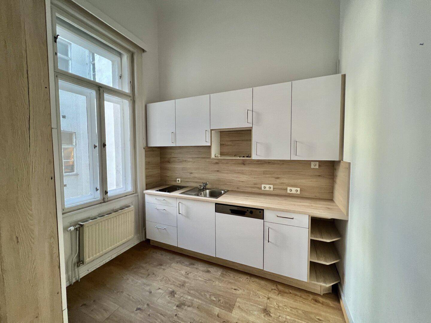 Funktionale Küchenzeile mit weißen Schränken, Holzarbeitsplatte und Fenster, ideal für kleine Büros.