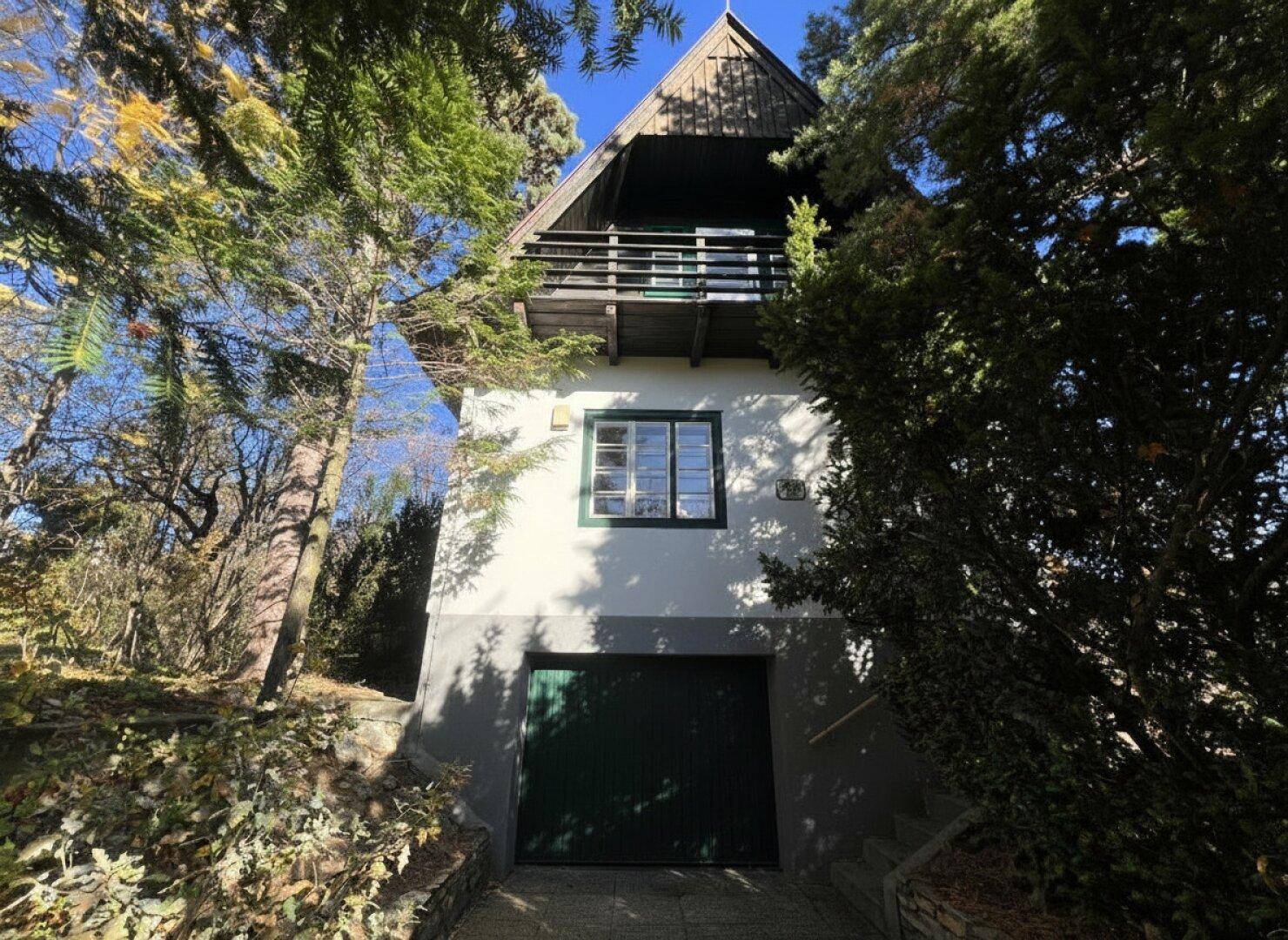 Traditionelles Haus mit Satteldach, Balkon und Garage, umgeben von Bäumen.