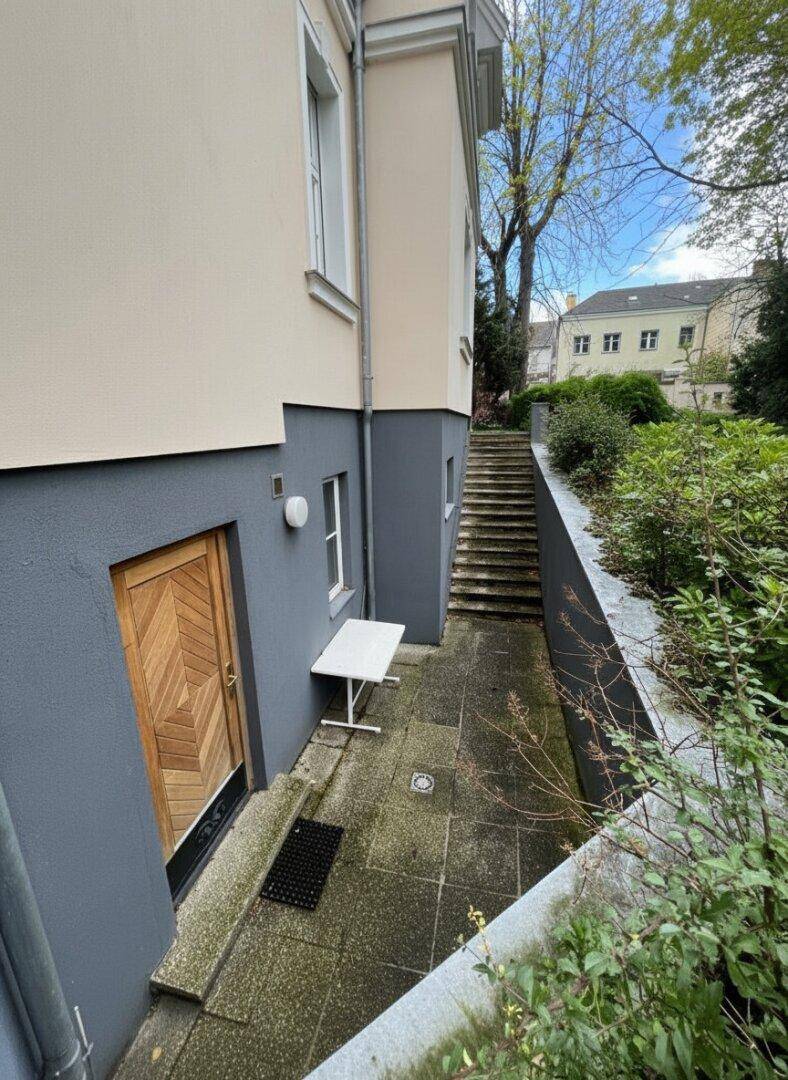 Seitlicher Eingangsbereich mit kleiner gepflasterter Terrasse und Treppe zum oberen Bereich.