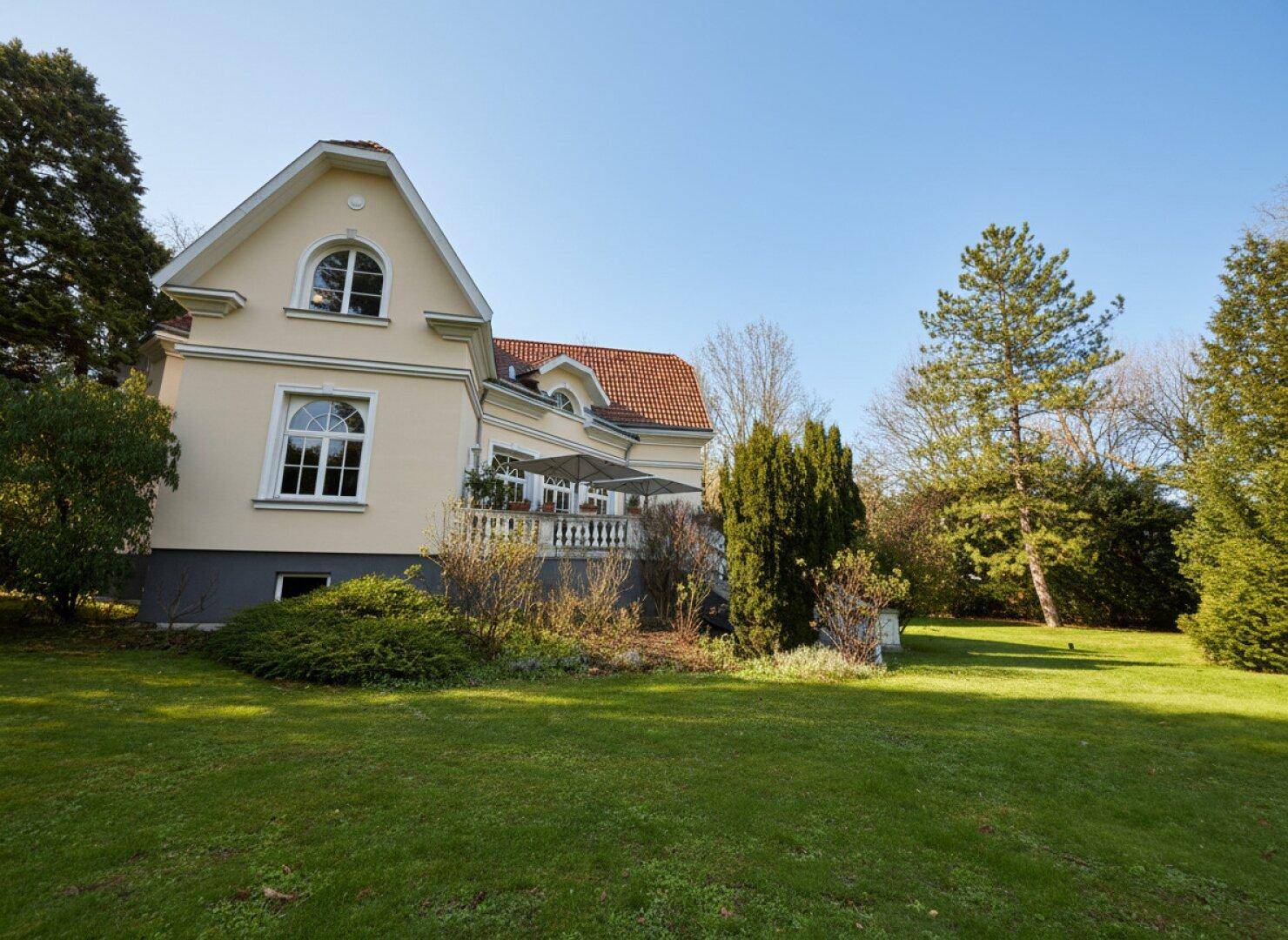 Seitliche Ansicht der Villa mit weitläufigem Rasen und gepflegten Bäumen im Garten.