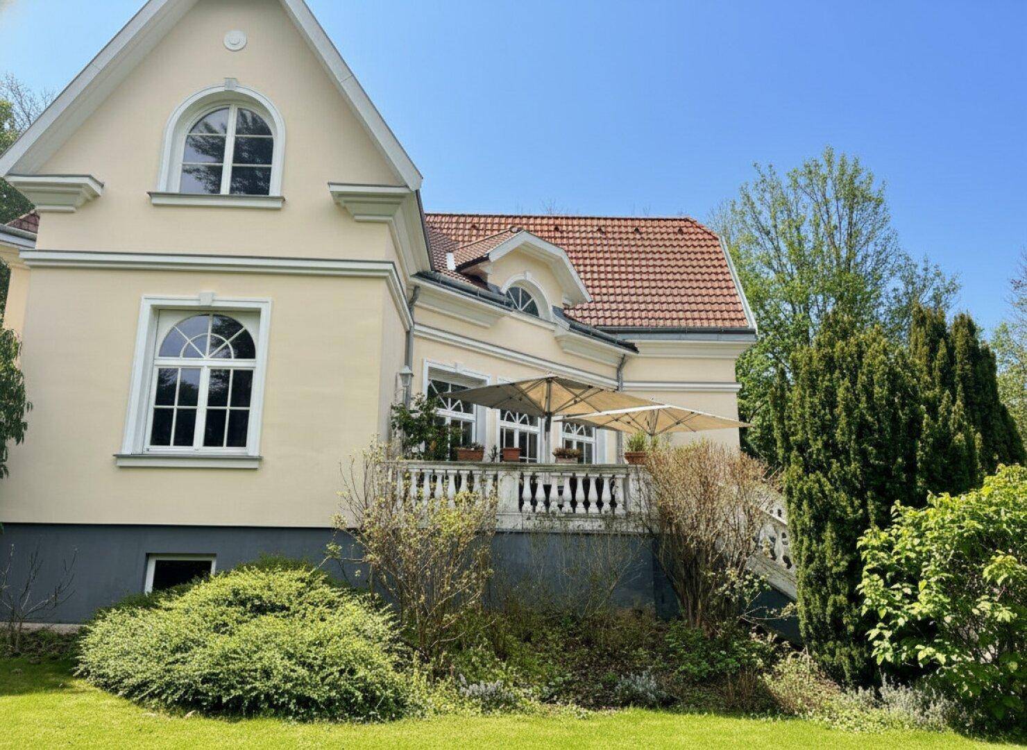 Sonniger Terrassenbereich mit Balustrade, Sonnenschirmen und Blick in den Garten.