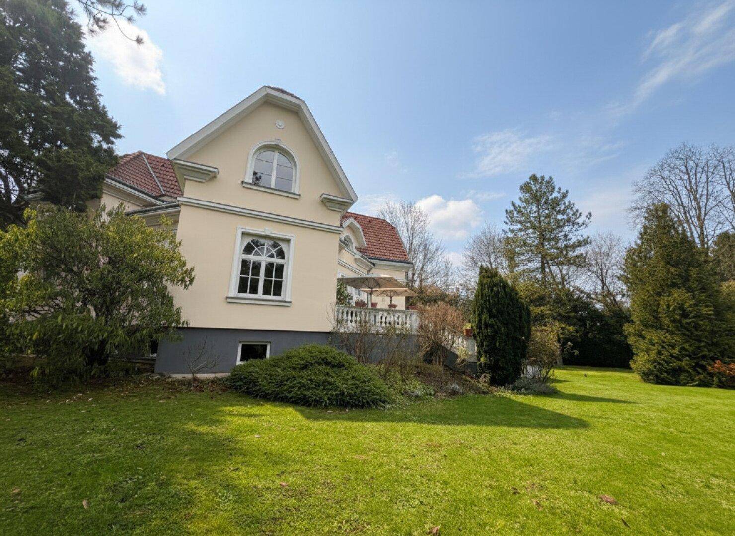 Weitläufiger Gartenbereich neben der Villa mit großem Rasen und altem Baumbestand.