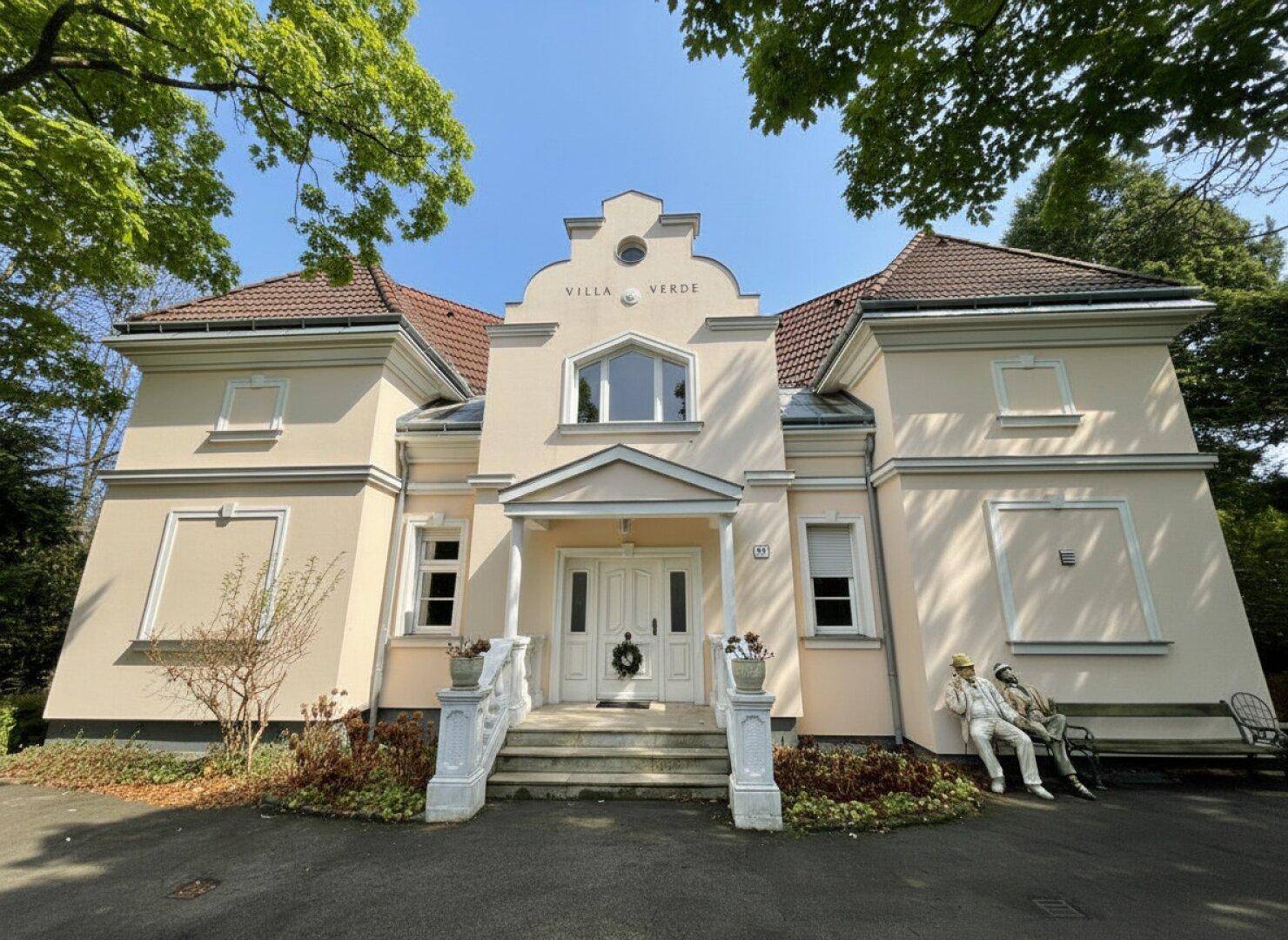 Elegante Villa mit klassischer Architektur, hellem Anstrich und gepflegtem Vorgarten.