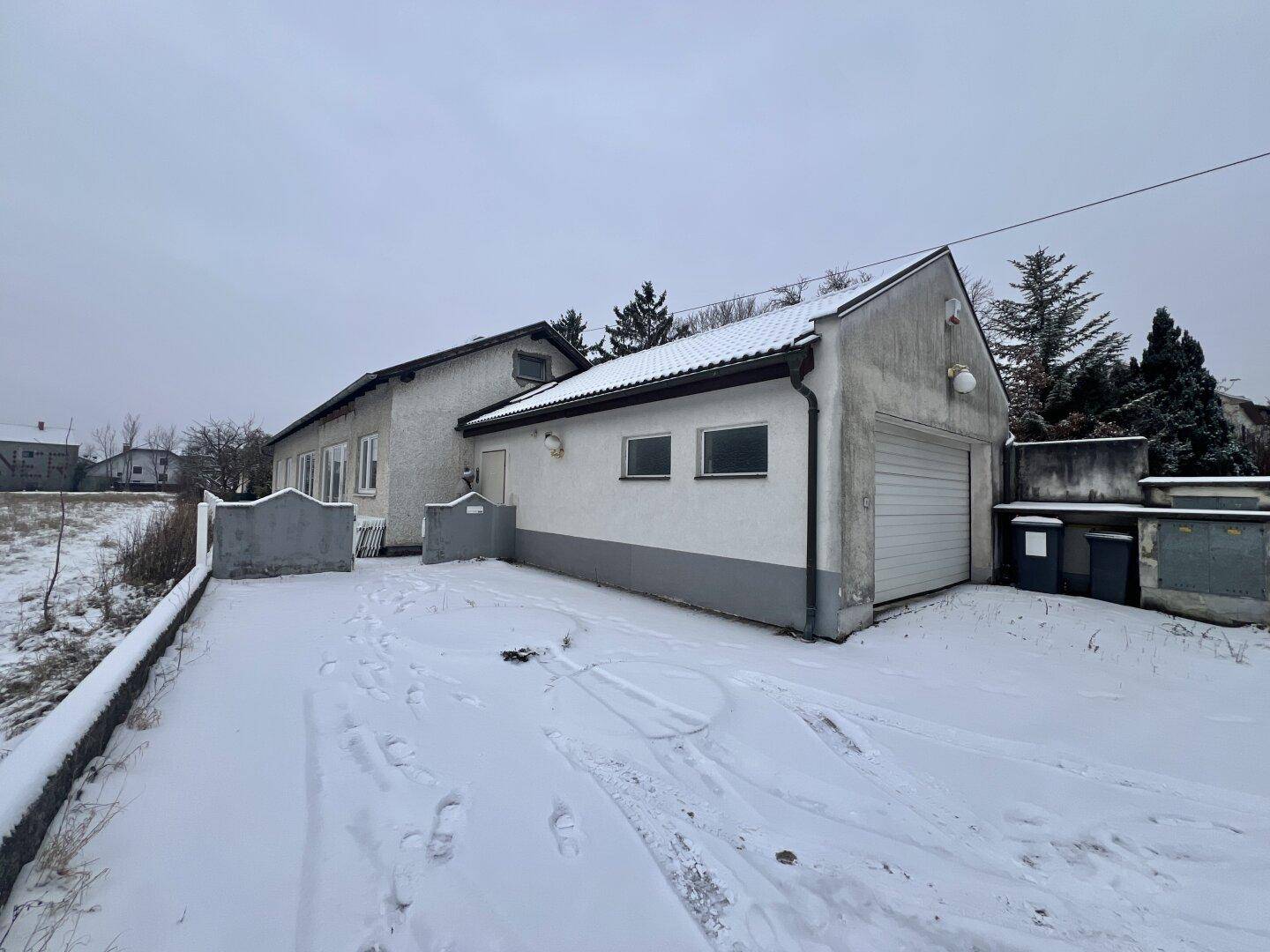 Hausfassade mit Garage und schneebedeckter Einfahrt an einem kalten Wintertag.