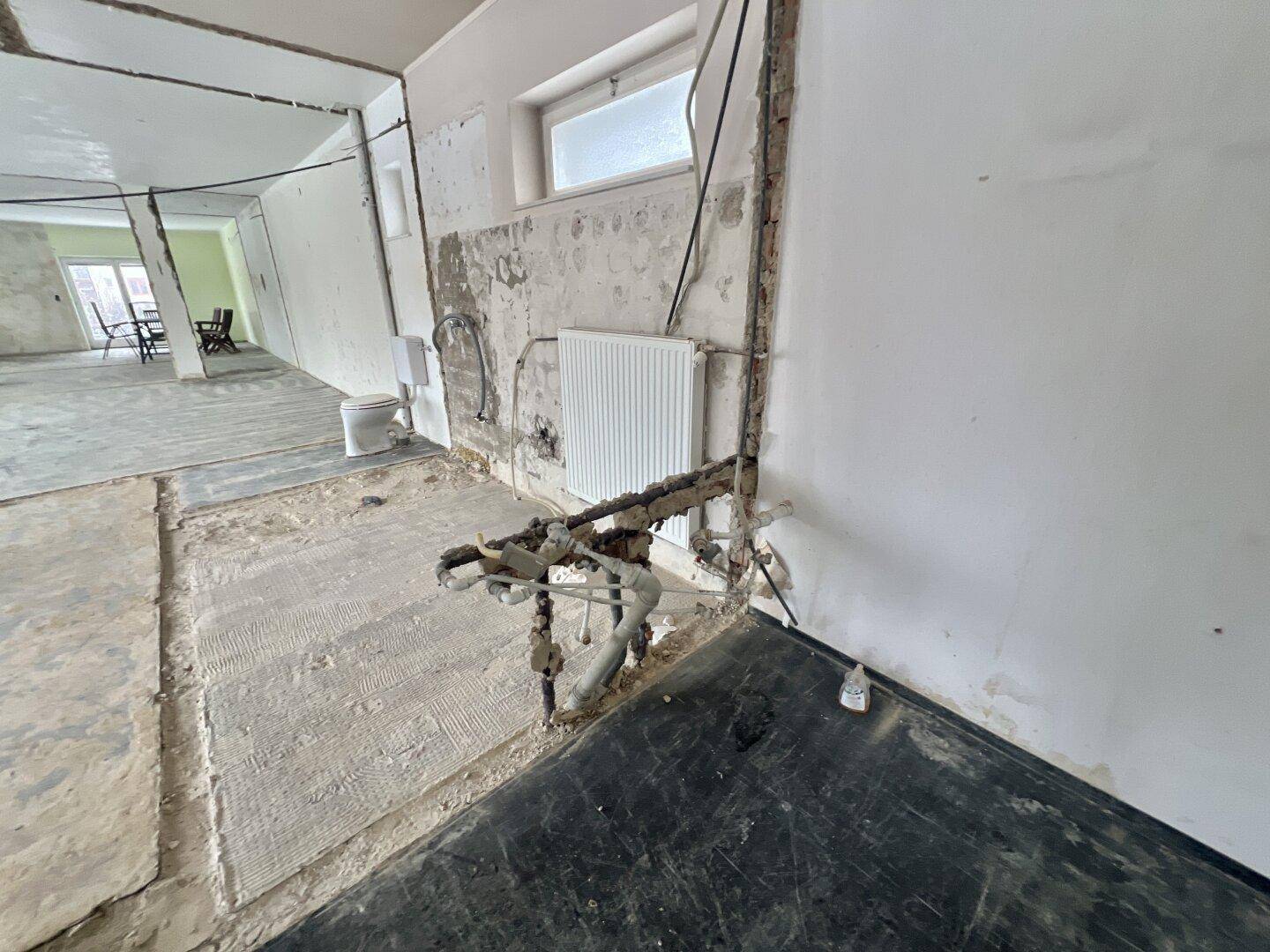 Detailansicht von freiliegenden Rohren und einem Heizkörper in einem Raum im Rohbau.