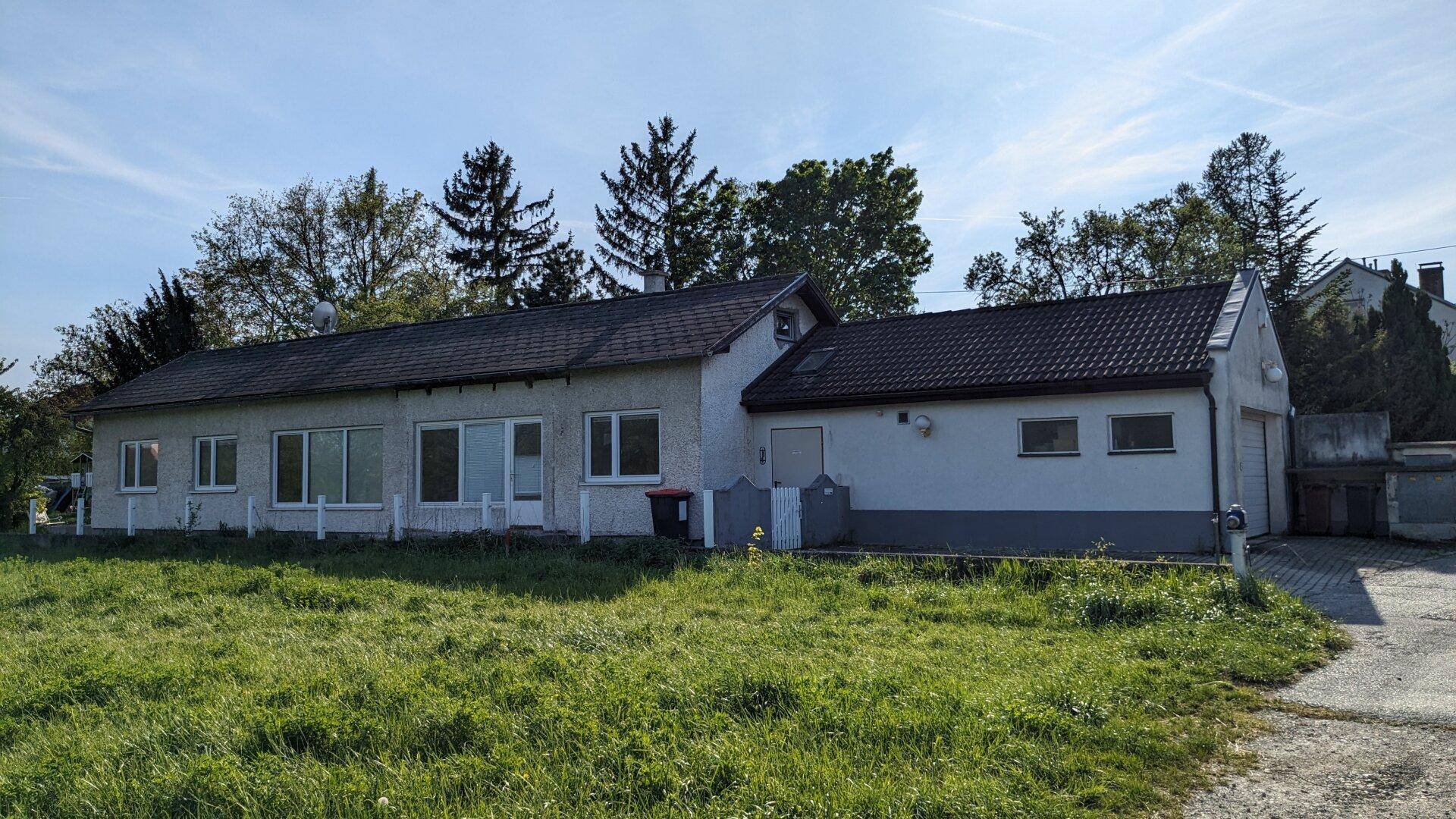 Hausfassade mit Garten und gepflastertem Bereich unter einem klaren, sonnigen Himmel.