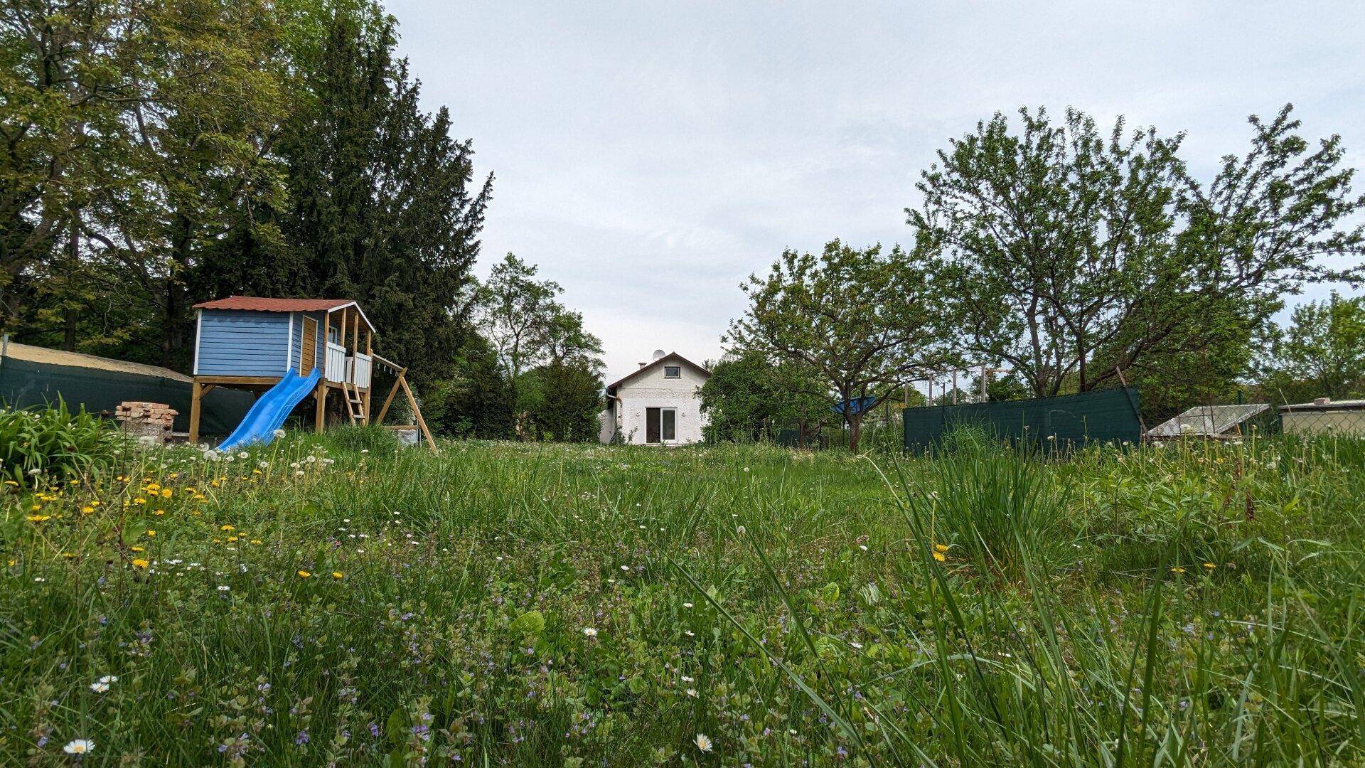 Weitläufiger Garten mit Spielplatz, hohen Bäumen und viel Grünfläche.