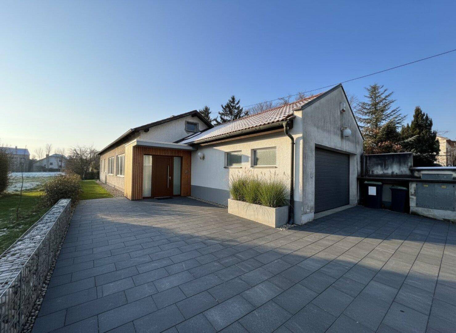 Hausfassade mit modernem Eingangsbereich, großer gepflasterter Einfahrt und Garage.