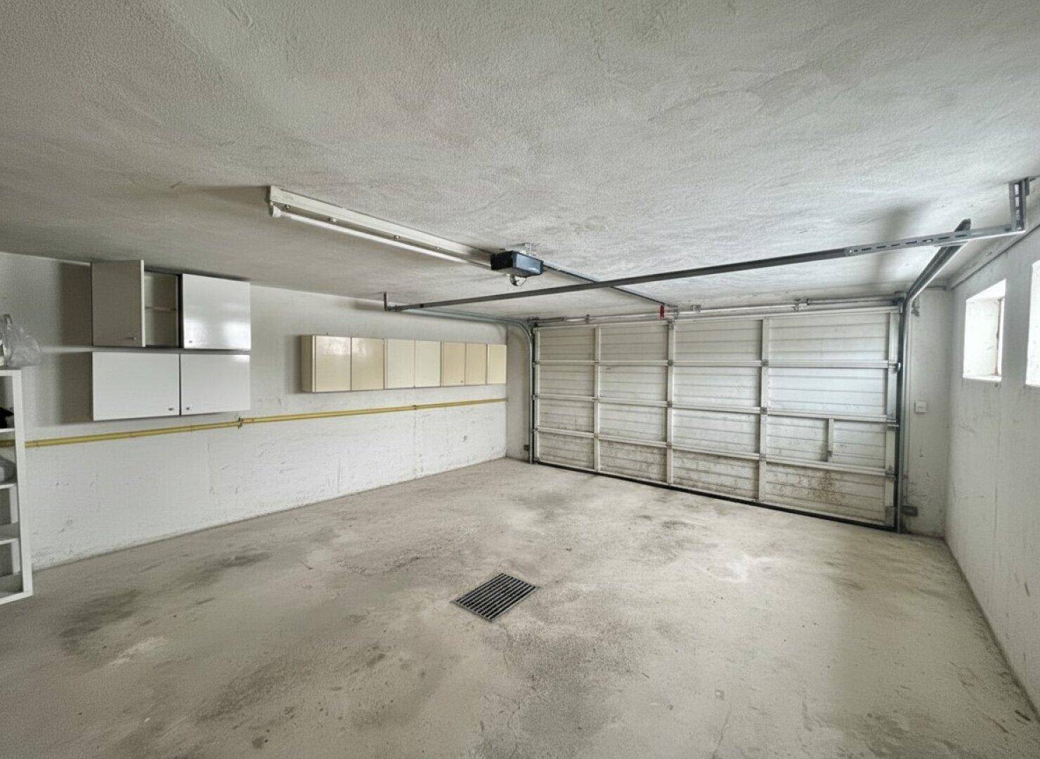 Geräumige Garage mit Rolltor, Betonboden und praktischen Wandschränken.
