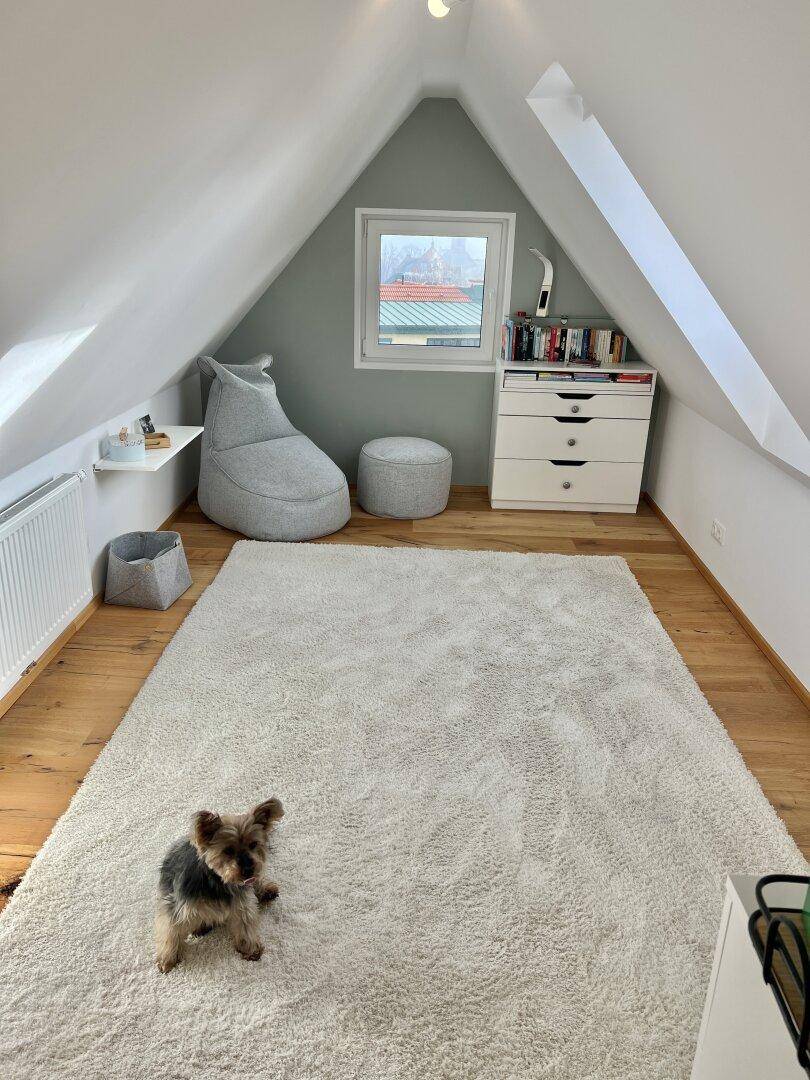 Gemütliches Dachgeschosszimmer mit Holzboden und kleinem Fenster, ideal als Kinder- oder Gästezimmer.