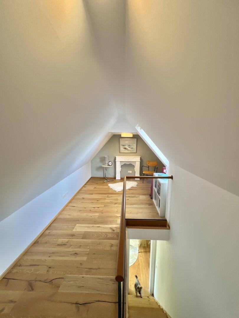 Heller Flur im Dachgeschoss mit Holzboden und Treppenabgang, führt zu einem weiteren Zimmer.