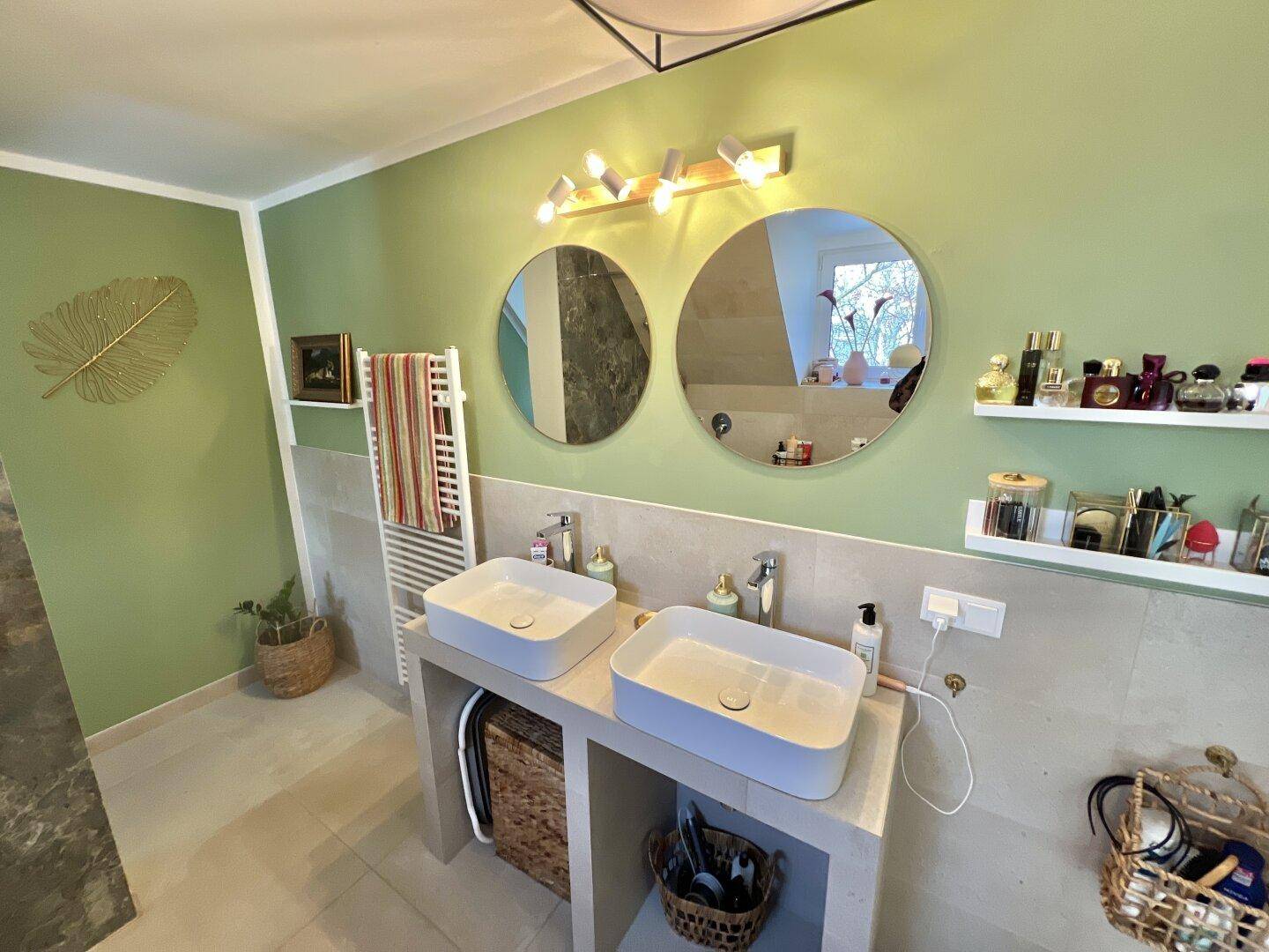 Modernes Badezimmer mit Doppelwaschbecken, grünen Wänden und beheiztem Handtuchhalter.