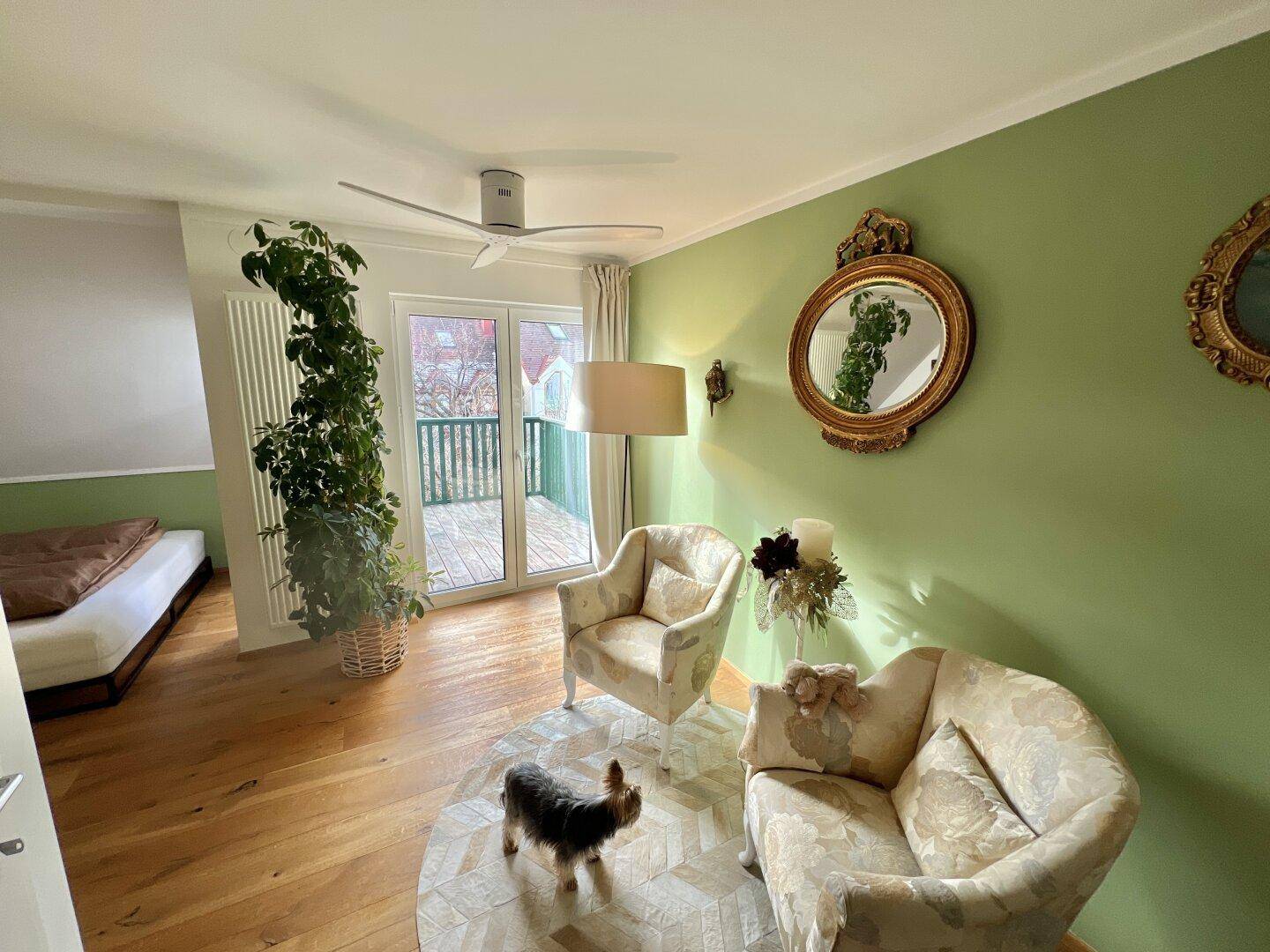 Helles Schlafzimmer mit grünen Wänden, Holzboden und Zugang zu einem Balkon.