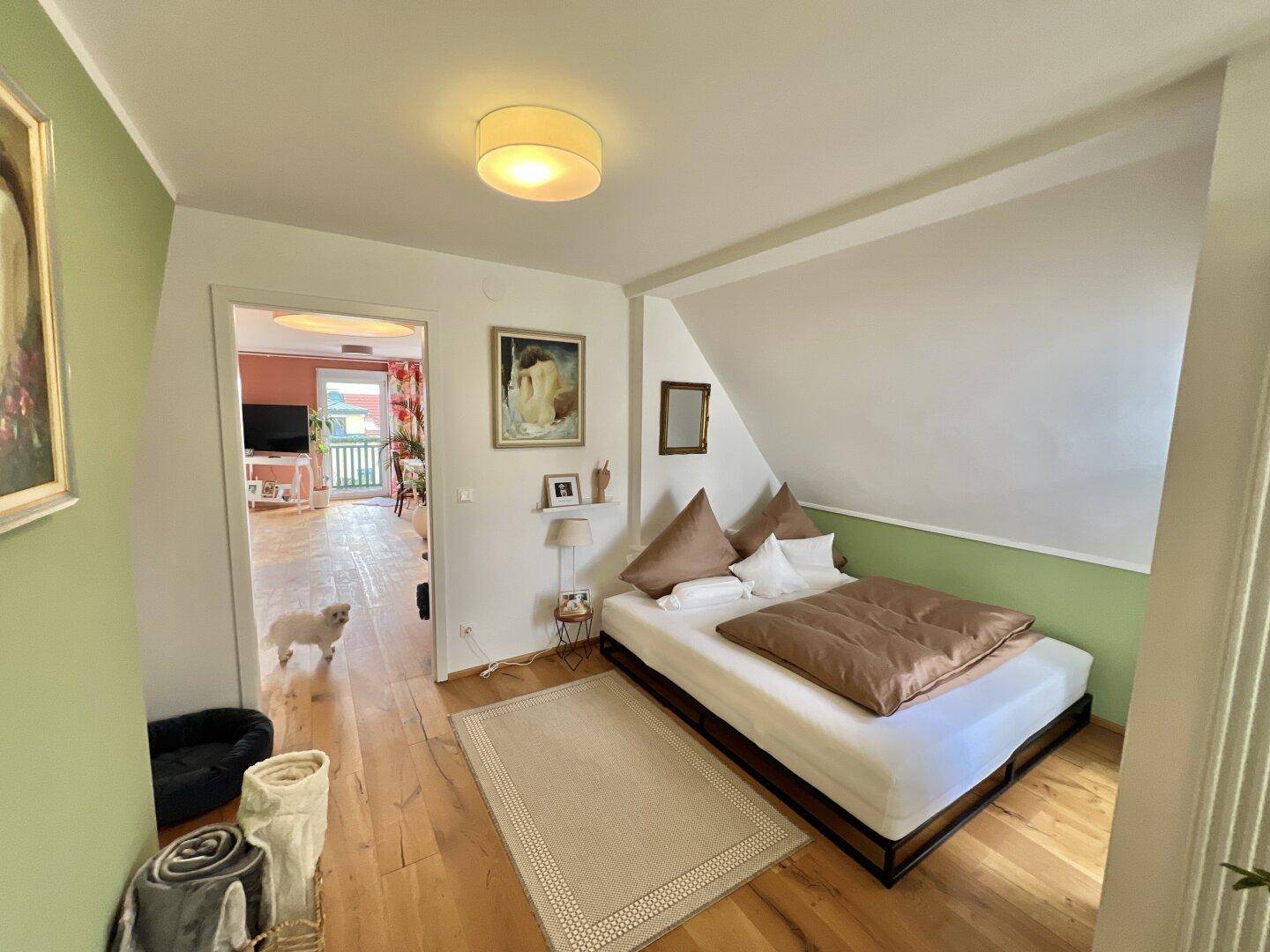 Helles Schlafzimmer im Dachgeschoss mit Holzboden und schrägen Wänden, gemütlich eingerichtet.