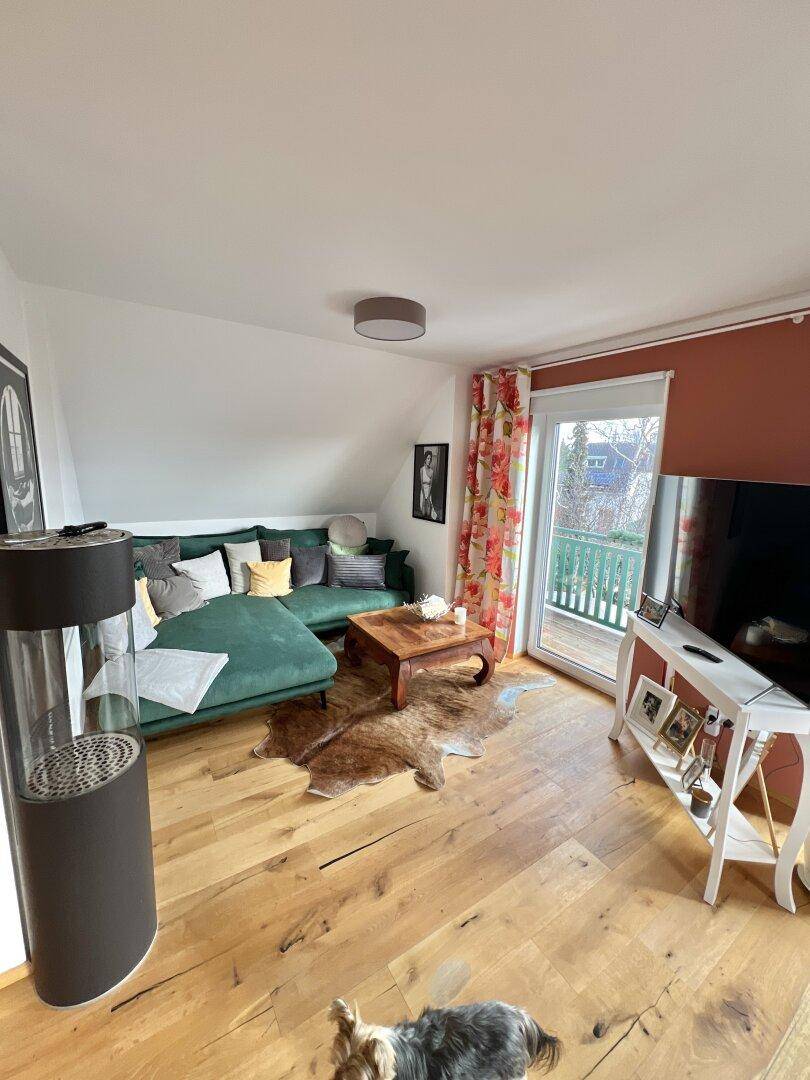 Gemütliches Wohnzimmer im Dachgeschoss mit Holzboden, Sofa und Zugang zum Balkon.