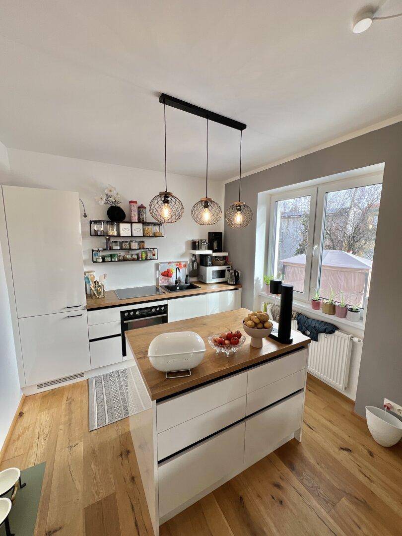 Moderne Küche mit Kücheninsel, Holzarbeitsplatte und Blick nach draußen durch das Fenster.