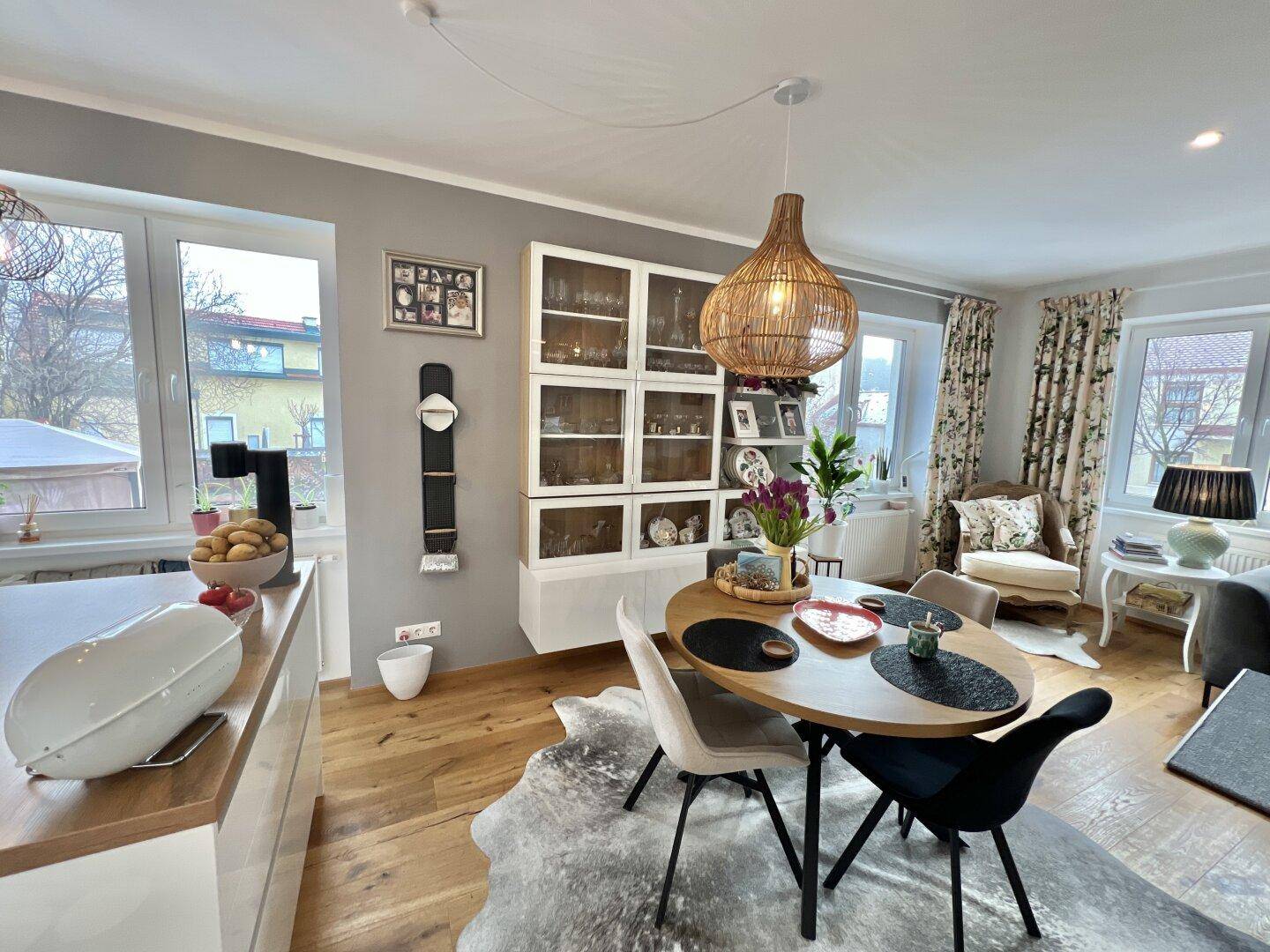 Gemütlicher Essbereich mit Holztisch und Rattanlampe, offen zum Wohnzimmer mit großen Fenstern.