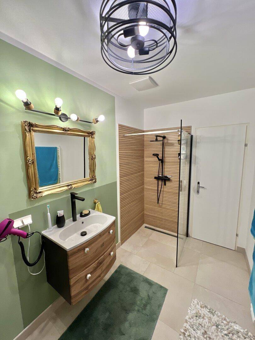 Modernes Badezimmer mit grünen Wänden, Holzdetails und einer geräumigen begehbaren Dusche.