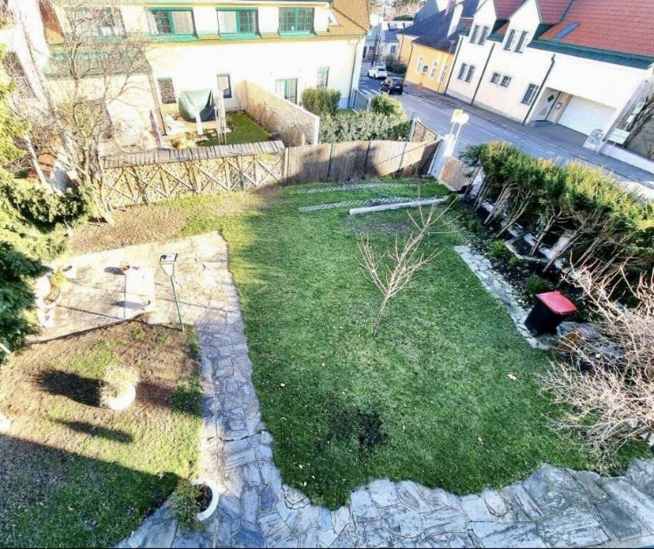 Gepflegter Gartenbereich mit Rasenfläche und Steinweg, umgeben von Hecken und Bäumen.
