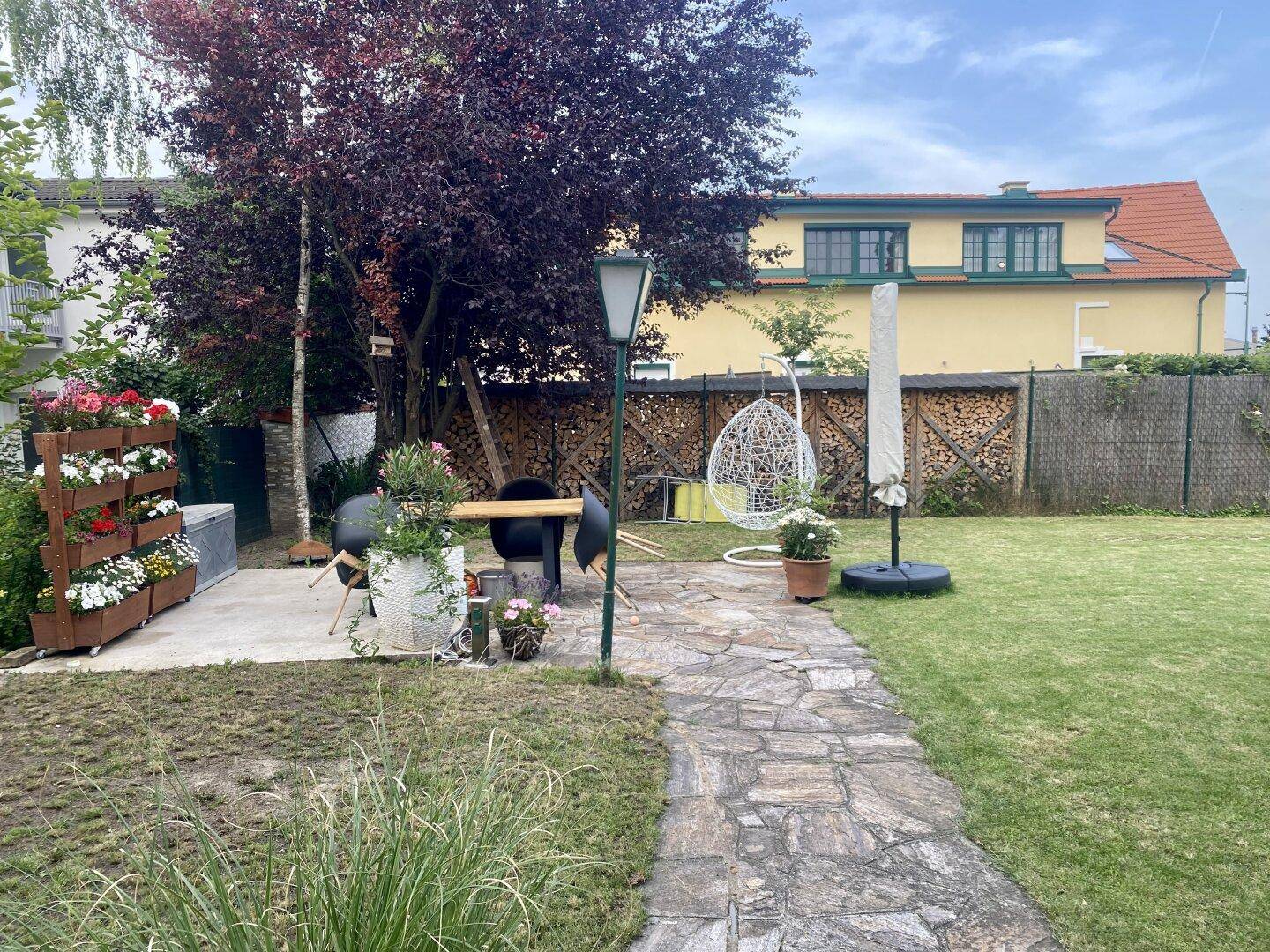 Gepflegter Garten mit Rasenfläche, Grillplatz und gemütlicher Hängesessel, ideal für Entspannung.