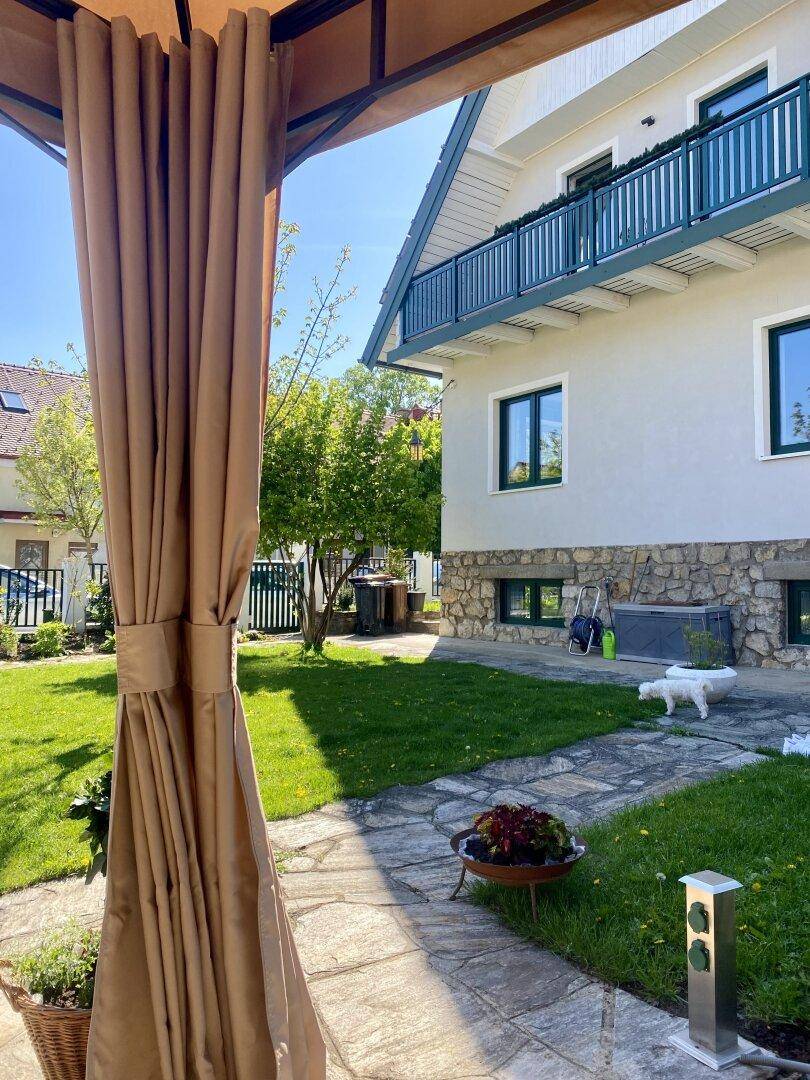 Gepflegter Gartenweg führt zum Haus, mit einem Pavillon und viel Grün.