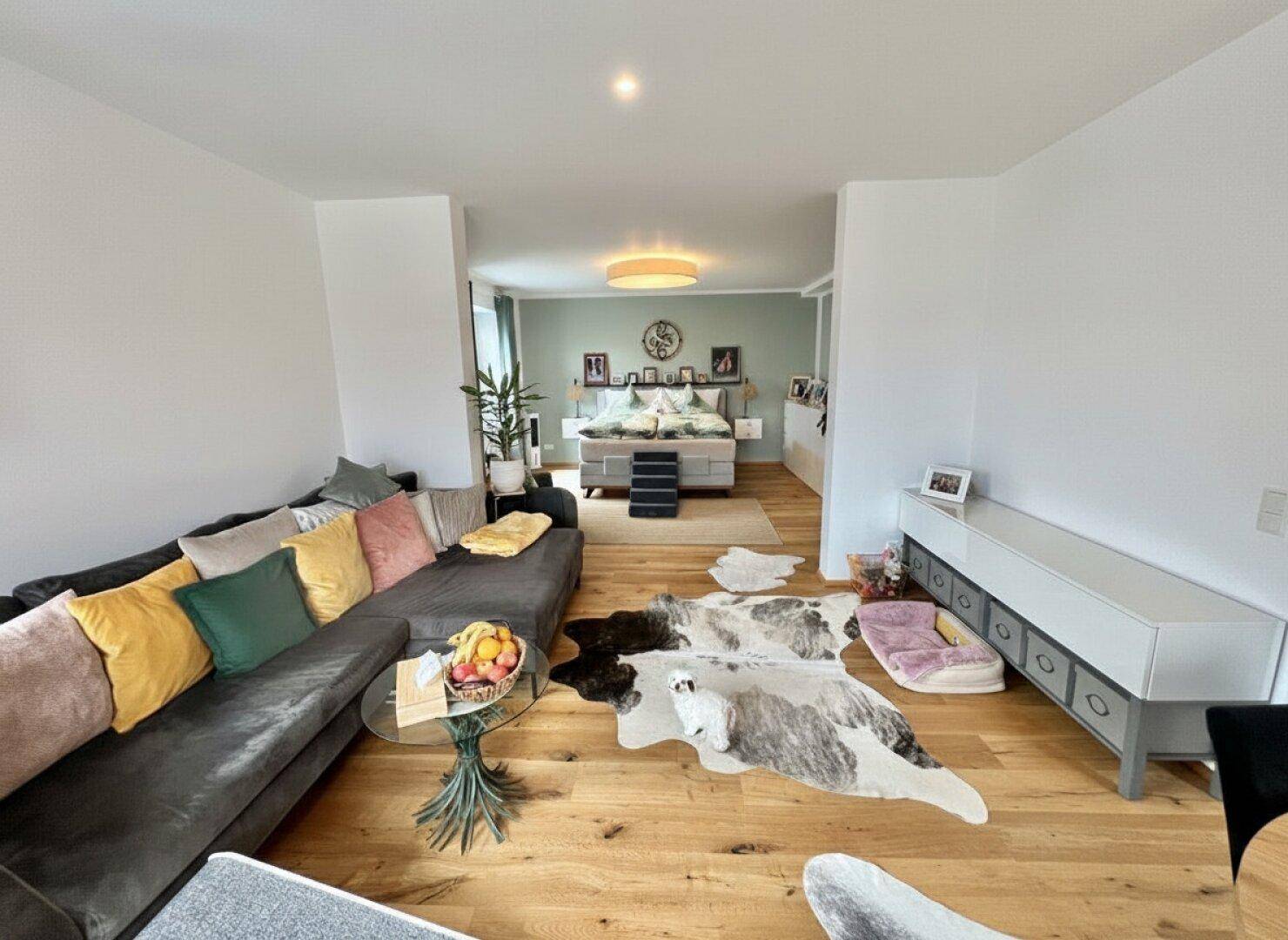 Komfortables Wohnzimmer mit großem Sofa und Holzboden, offen zum Schlafbereich.