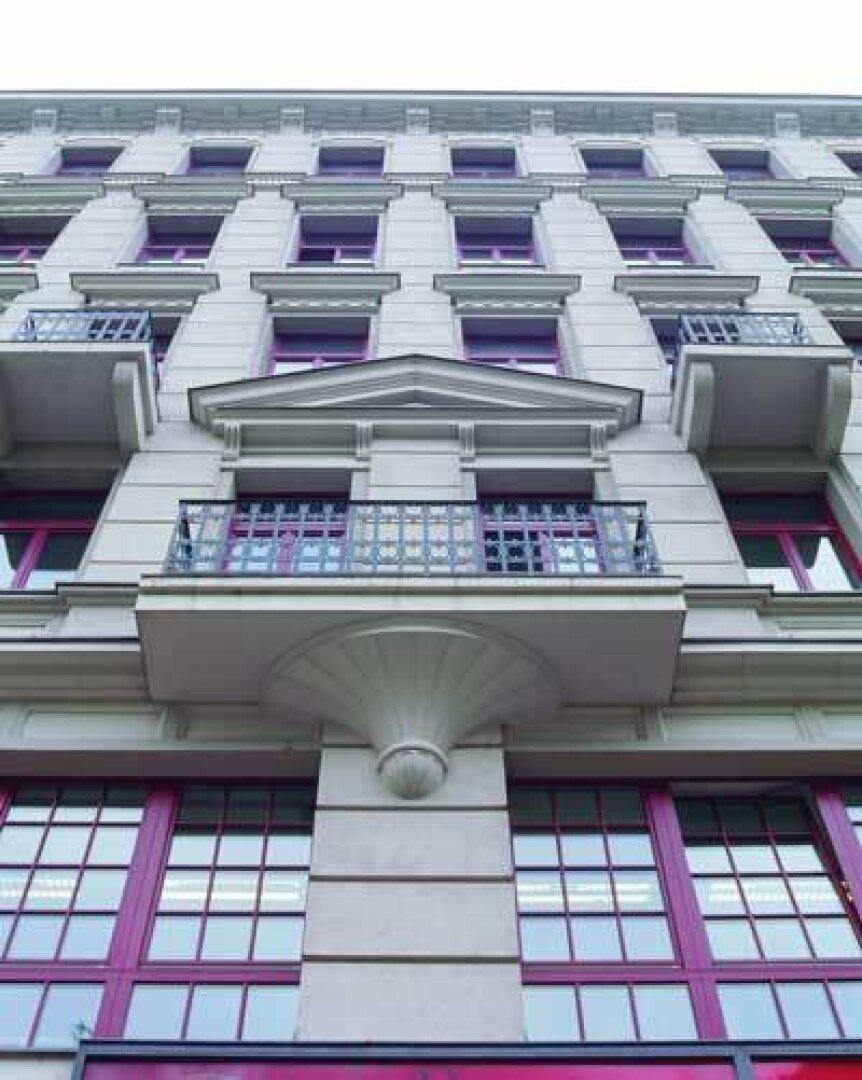 Detailansicht einer klassischen Gebäudefassade mit verzierten Balkonen und roten Fensterrahmen.