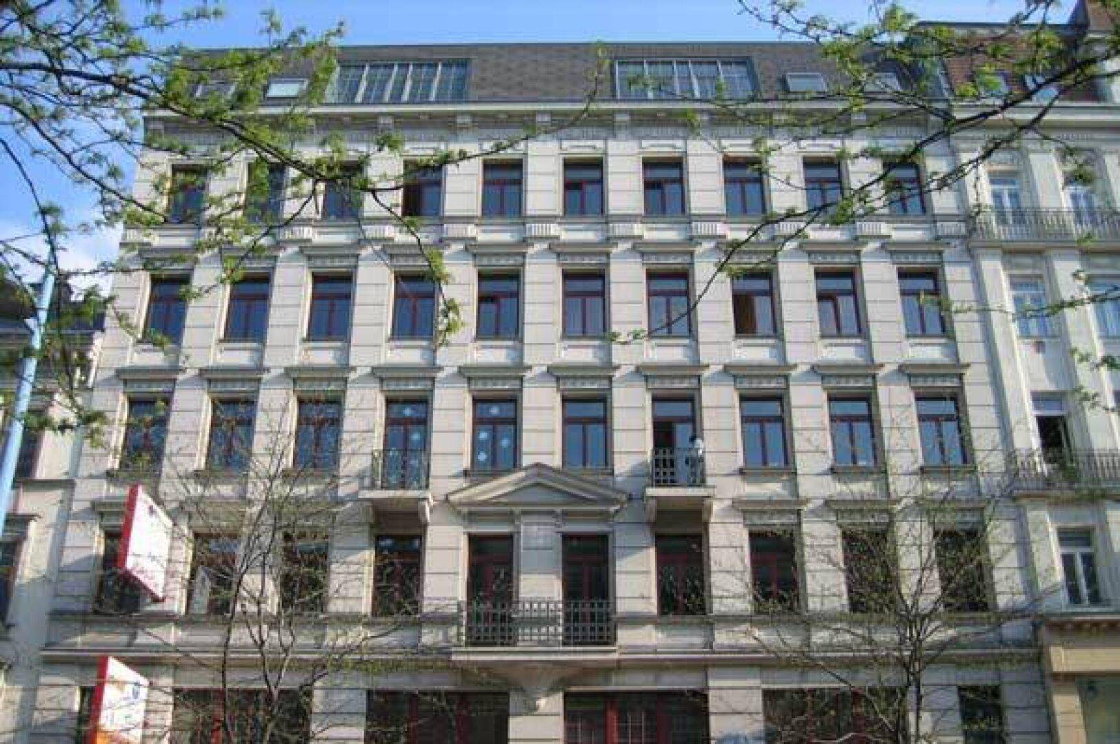 Klassische Fassade eines Mehrfamilienhauses mit vielen Fenstern und Balkonen unter blauem Himmel.