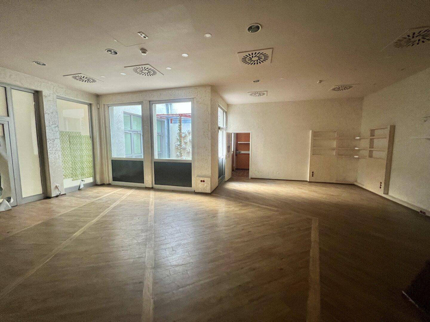 Heller Gewerberaum mit Holzboden, großen Fenstern und Blick auf einen Innenhof, ideal für Laden oder Büro.