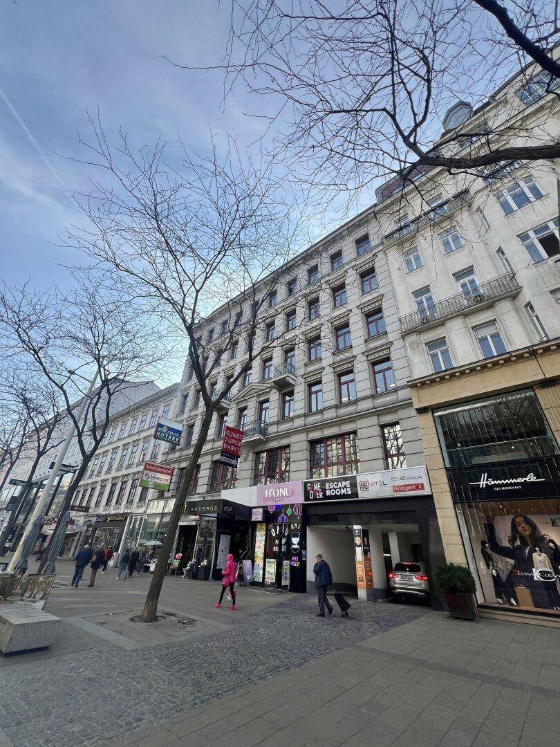 Historisches Gebäude mit mehreren Etagen und Geschäften im Erdgeschoss, an einer belebten Straße gelegen.