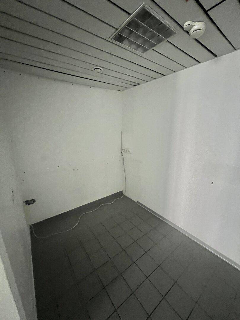 Kleiner Abstellraum mit dunklen Fliesen, weißen Wänden und einer Deckenplatte mit Lüftungsgitter.
