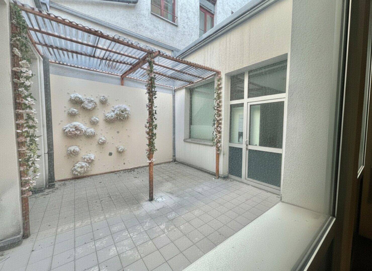 Innenhof mit gefliestem Boden, einer Pergola und dekorativen Wandelementen, bietet einen ruhigen Außenbereich.
