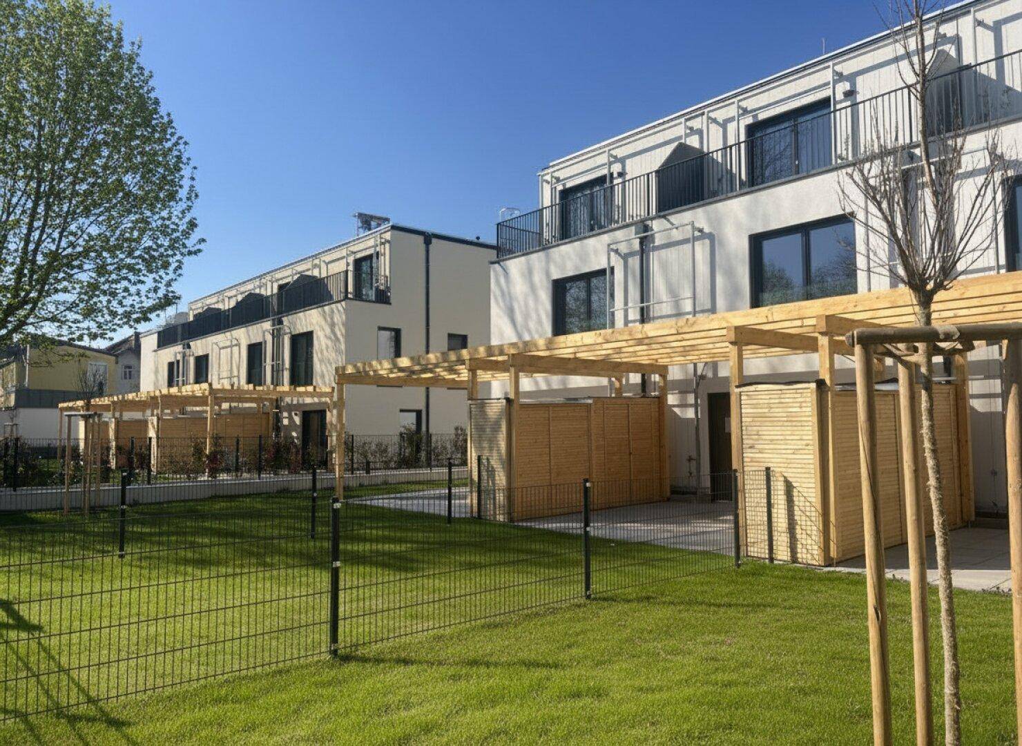 Neu gebaute Reihenhäuser mit grünen Gärten und Holzpergolen für Terrassenbereiche.