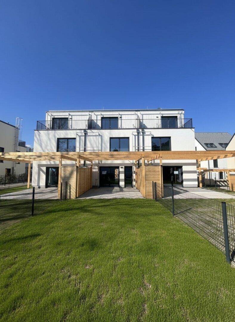 Moderne Reihenhäuser mit großzügigen Terrassen und privaten Gärten unter klarem Himmel.