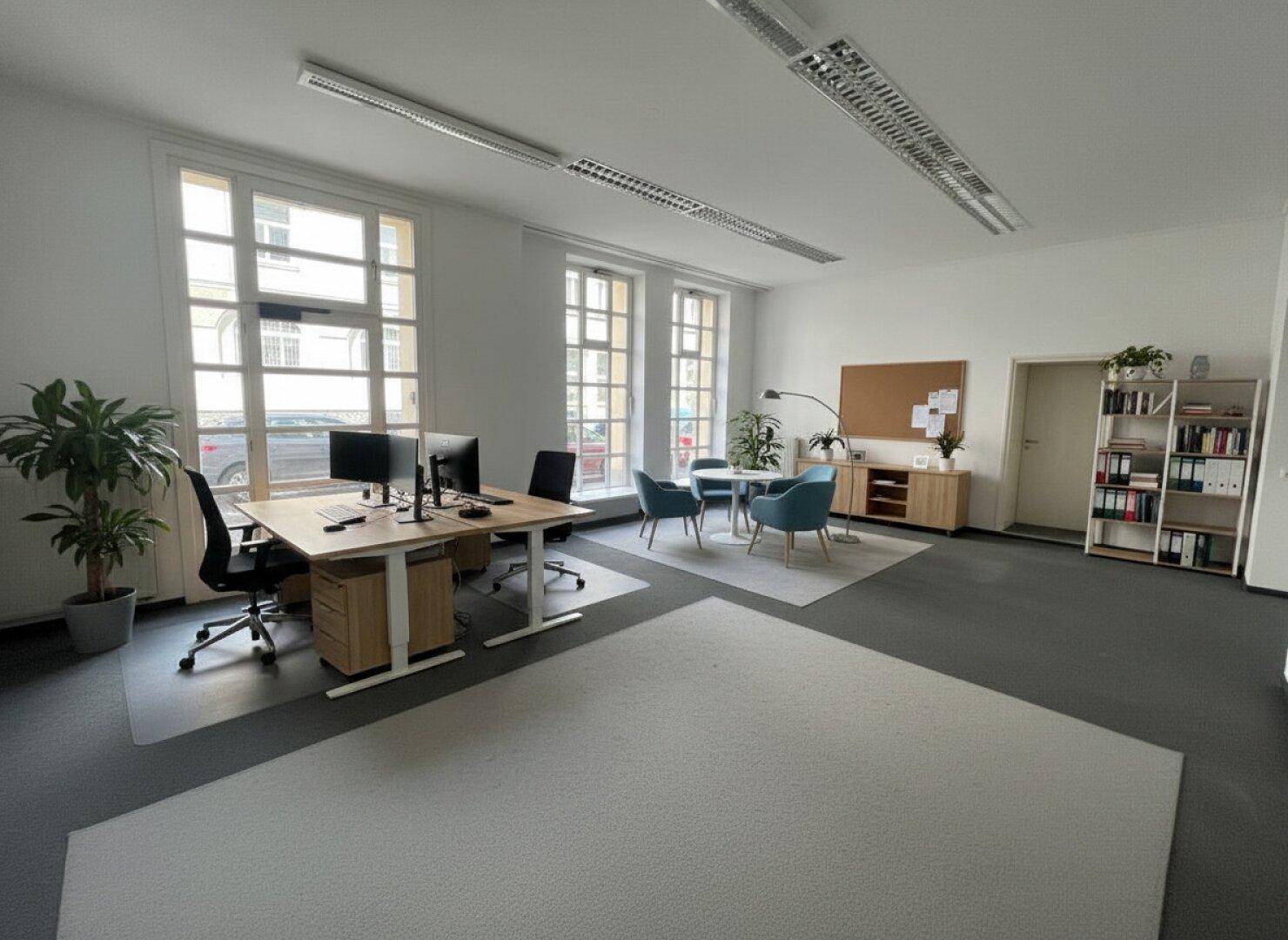 Modernes Büro mit Arbeitsplätzen, Besprechungsbereich und großen Fenstern, ausgestattet mit Teppichboden.
