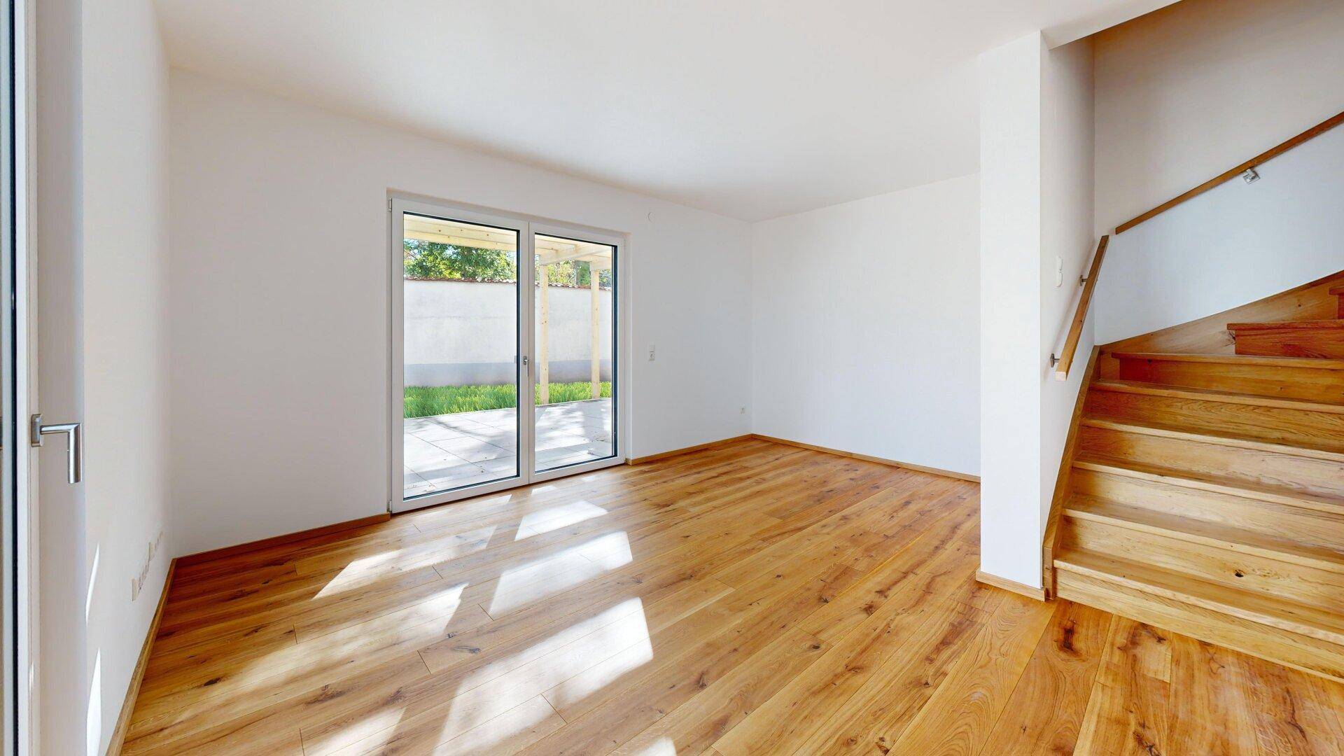 Helles, leeres Wohnzimmer mit Holzboden und Zugang zur Terrasse durch große Schiebetüren.