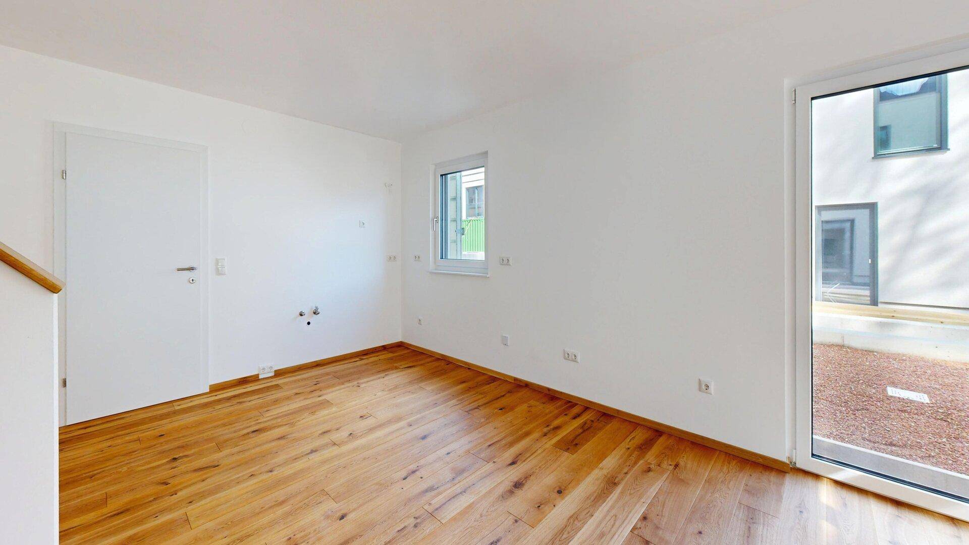 Heller Raum mit Holzboden und vorbereiteten Anschlüssen für eine Küche, mit Zugang nach draußen.