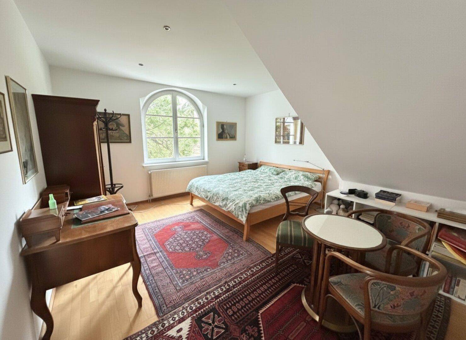 Gemütliches Schlafzimmer im Dachgeschoss mit Parkettboden, Rundbogenfenster und Schrägen.