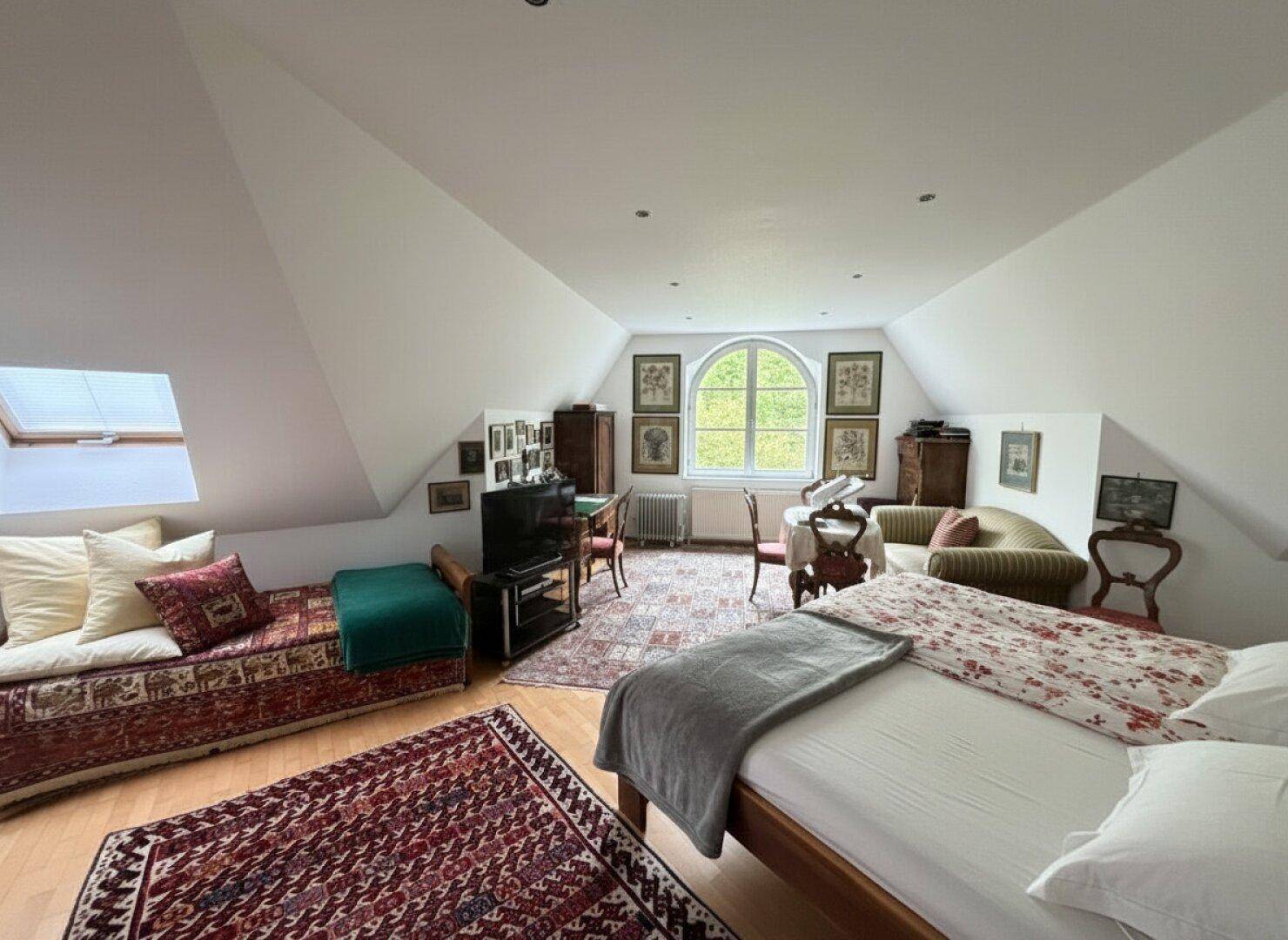 Großes Schlafzimmer im Dachgeschoss mit Parkettboden, Dachfenster und Rundbogenfenster.